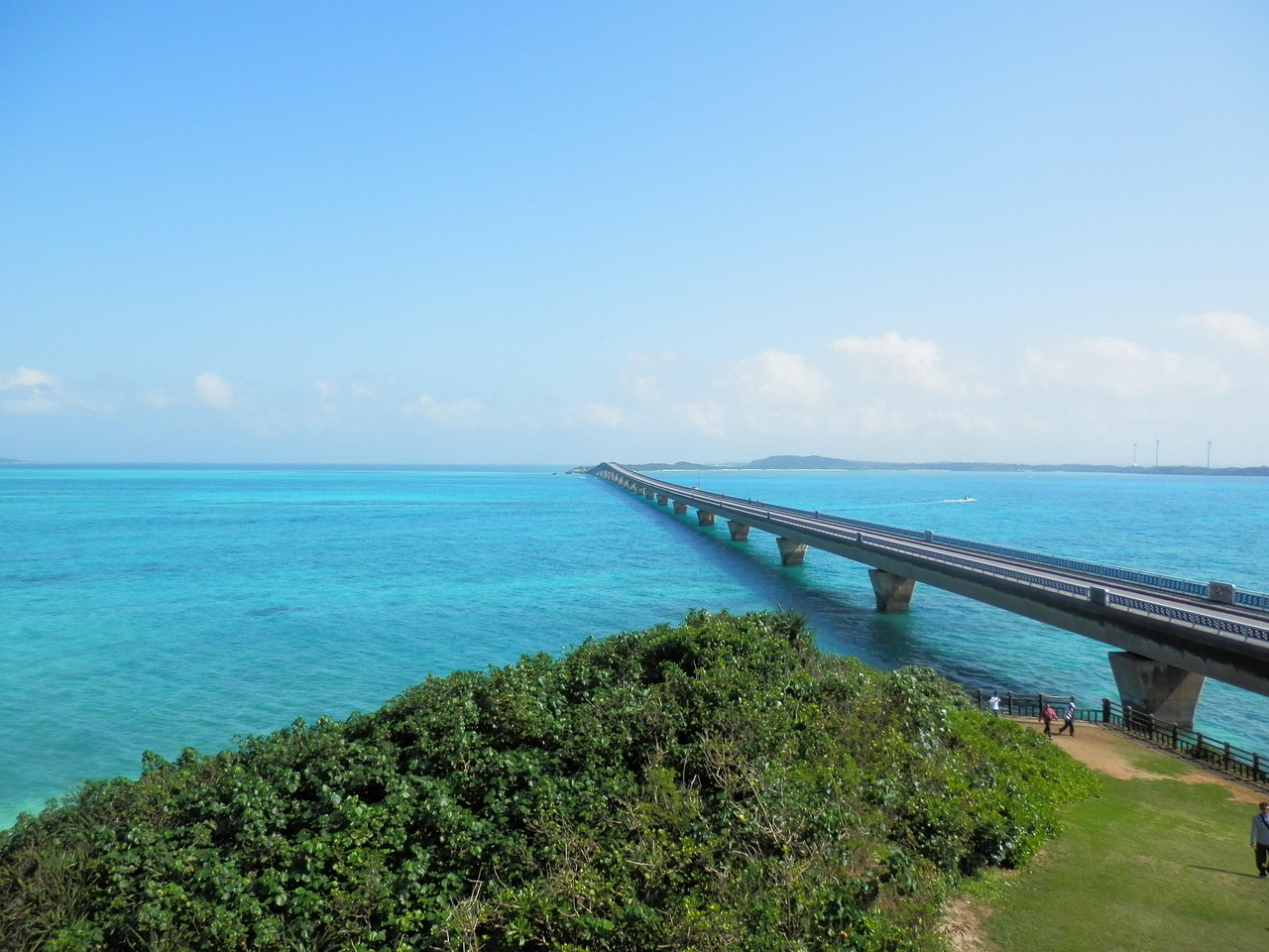A long bridge running across bright turquoise sea towards a low green island in the Miyako Islands