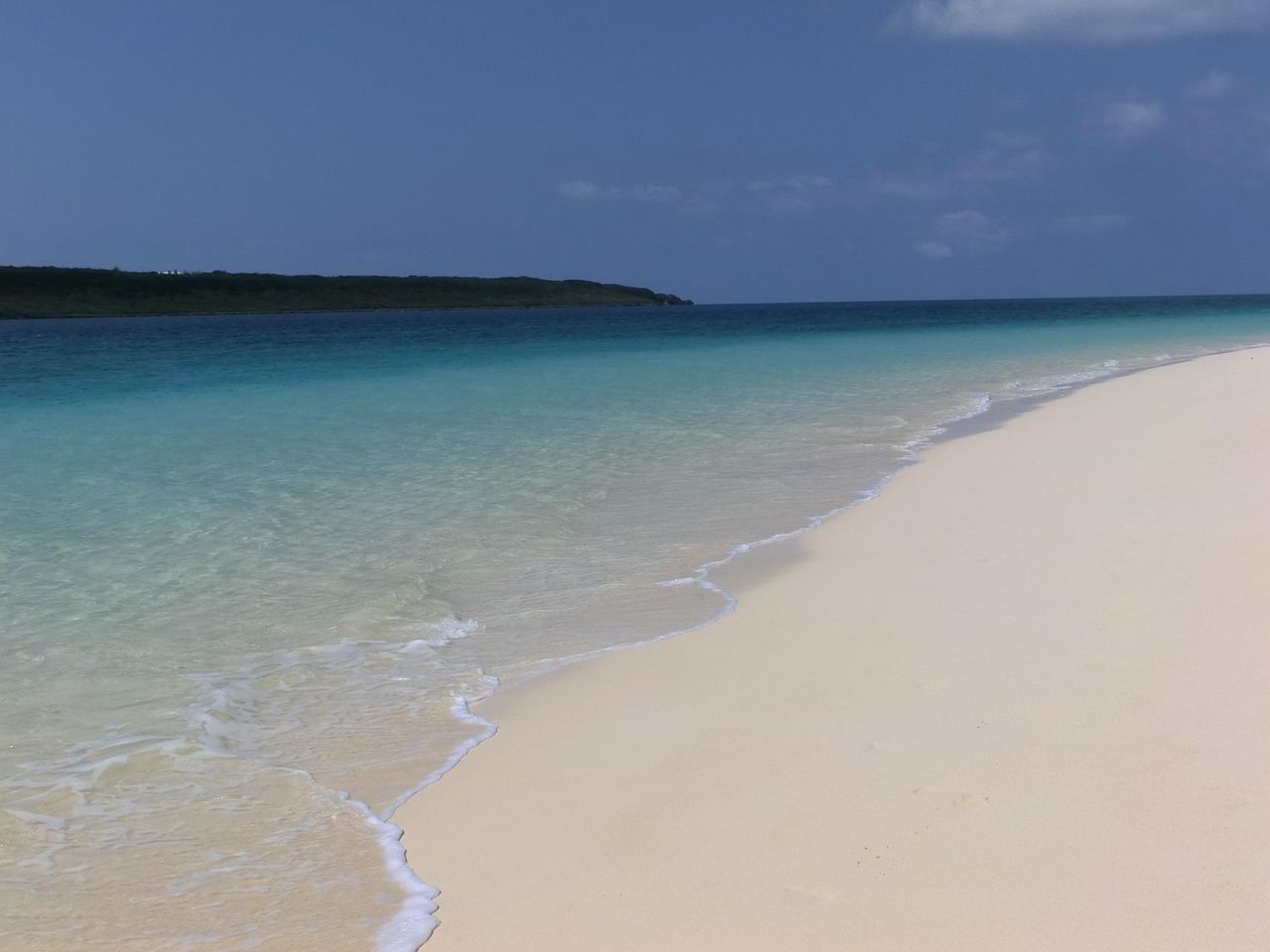 A white-sand beach with clear water and a low island beyond on Miyakojima
