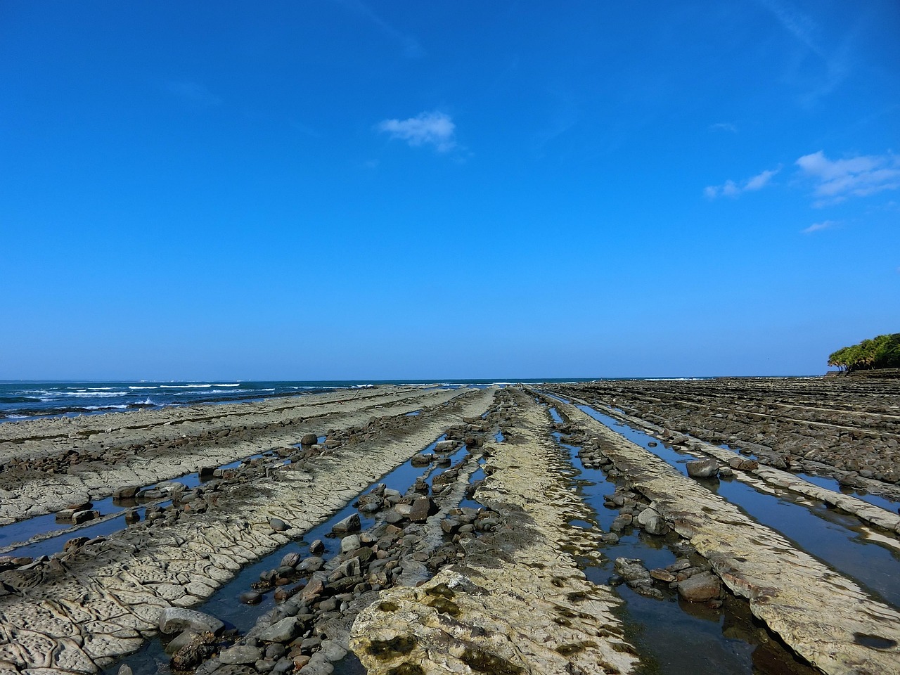 Long parallel ridges of grey rock running out to the sea at low tide at the Devil's Washboard, Aoshima, under a clear blue sky