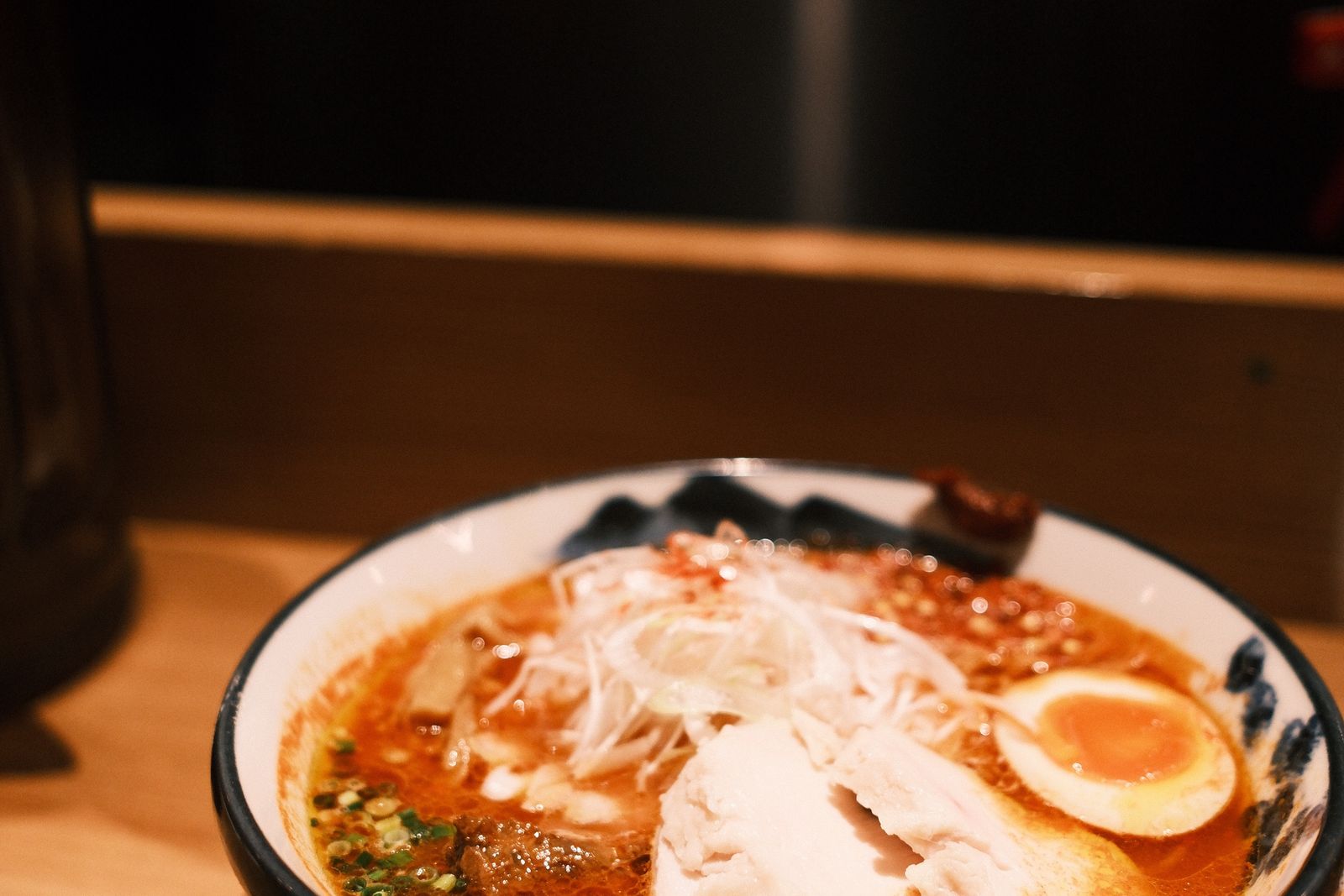 A dark red spicy ramen bowl topped with minced meat and greens.