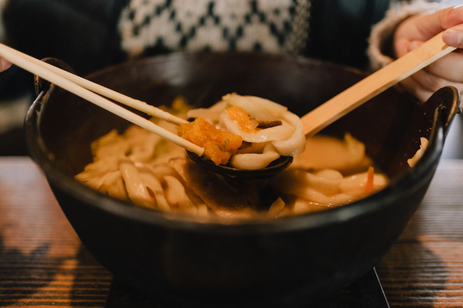 Udon noodles in dark broth in a dark bowl with chopsticks resting across it.