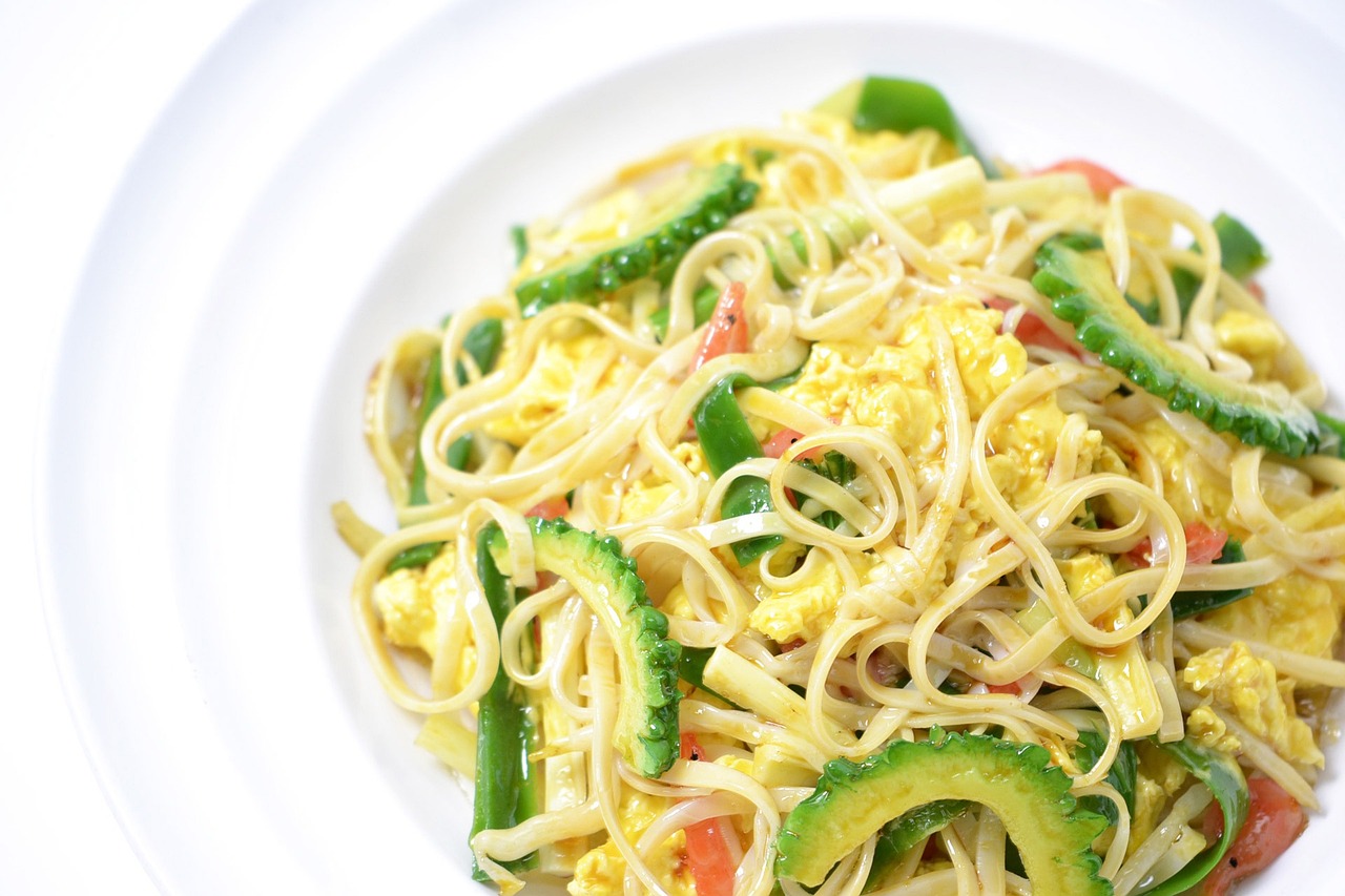 Stir-fried noodles with slices of bitter gourd and egg on a white plate