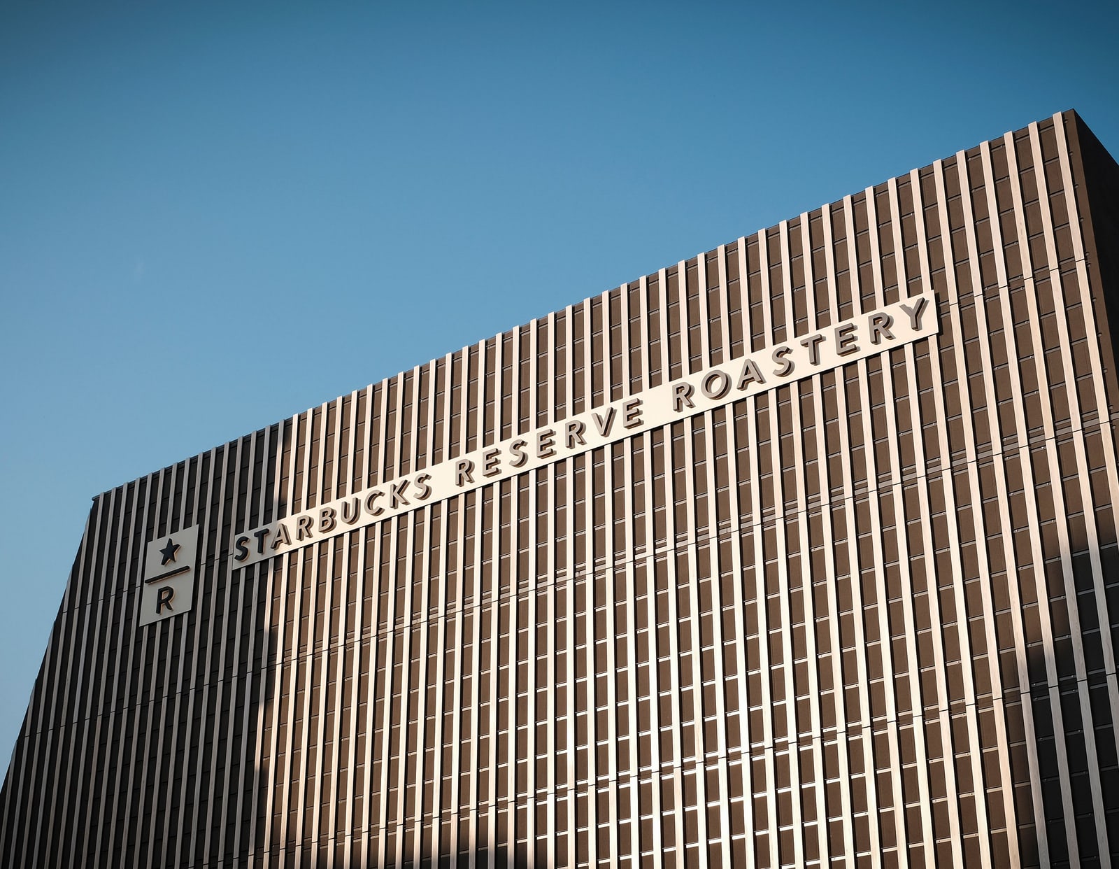 The louvred wooden facade of Starbucks Reserve Roastery Tokyo with its name sign, under a clear blue sky