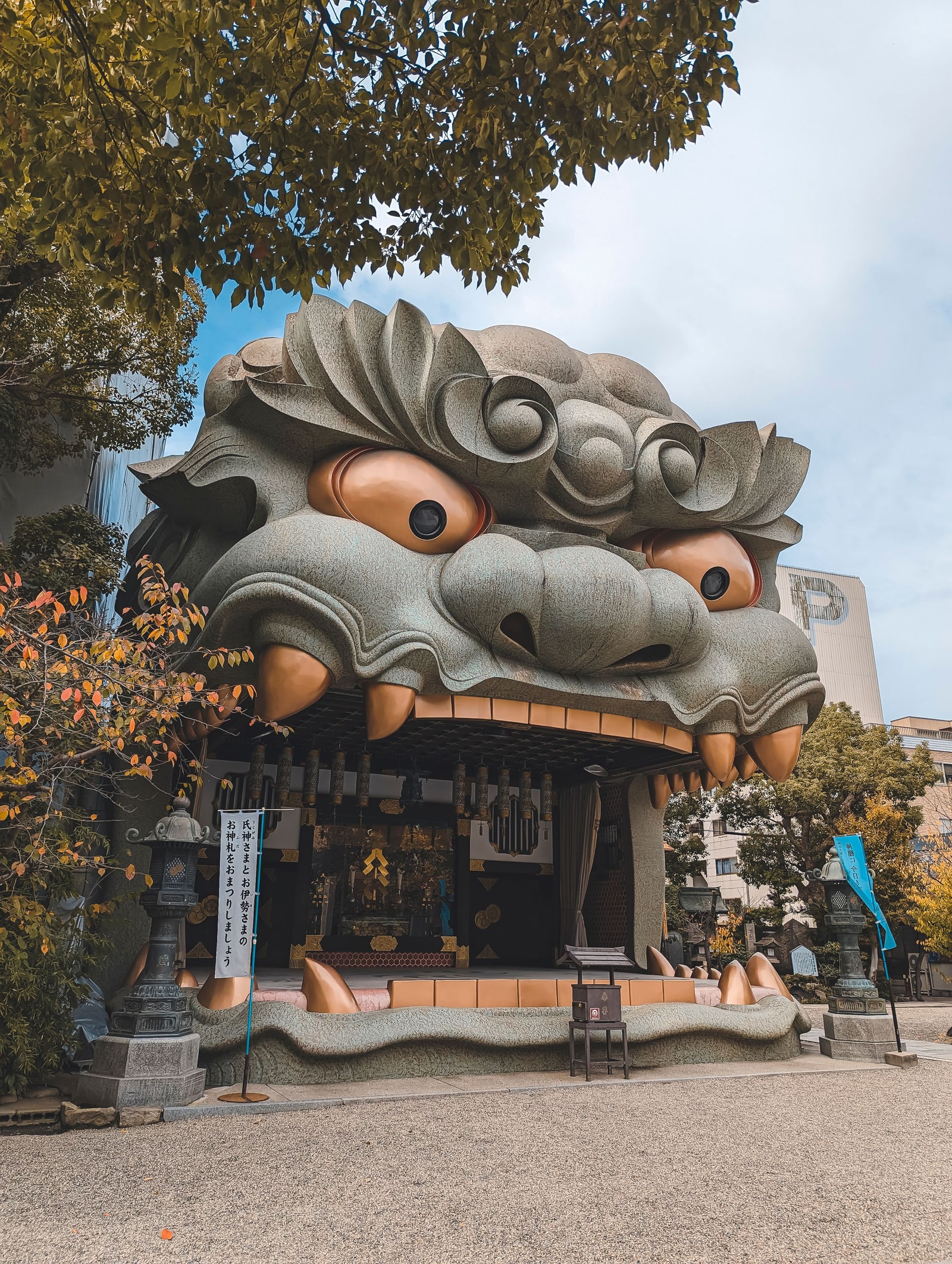 The lion-head hall of Namba Yasaka Shrine seen from the gravel courtyard, with stone lanterns on either side and autumn leaves at left