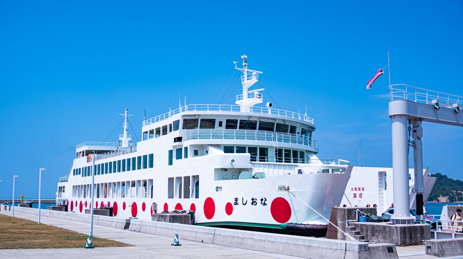 A white car ferry painted with large red dots, moored at a quay under a deep blue sky