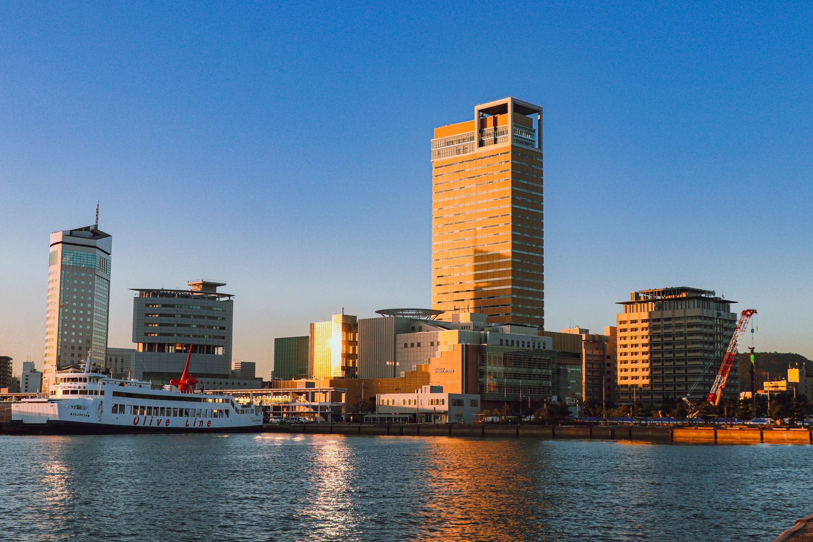 The Takamatsu harbour front in evening light, a tall square-crowned tower behind a ferry moored at the quay