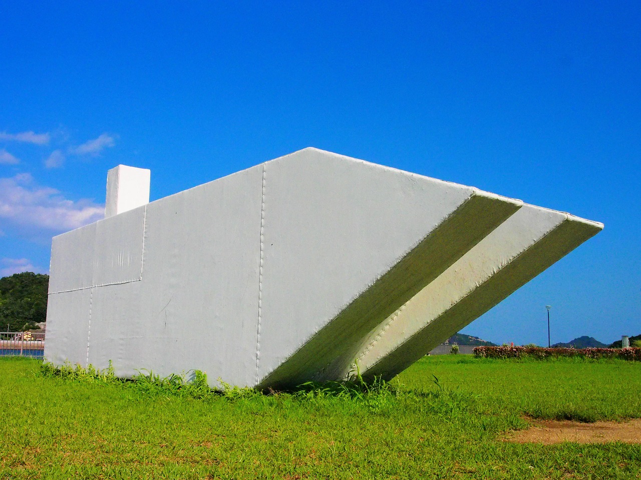 A white ship-shaped sculpture on a grass lawn under a blue sky