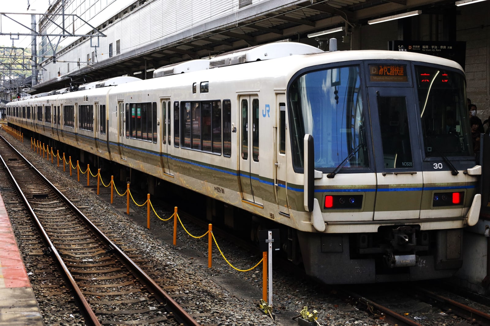 A cream JR commuter train with a blue and brown stripe at a platform at Kyoto Station.