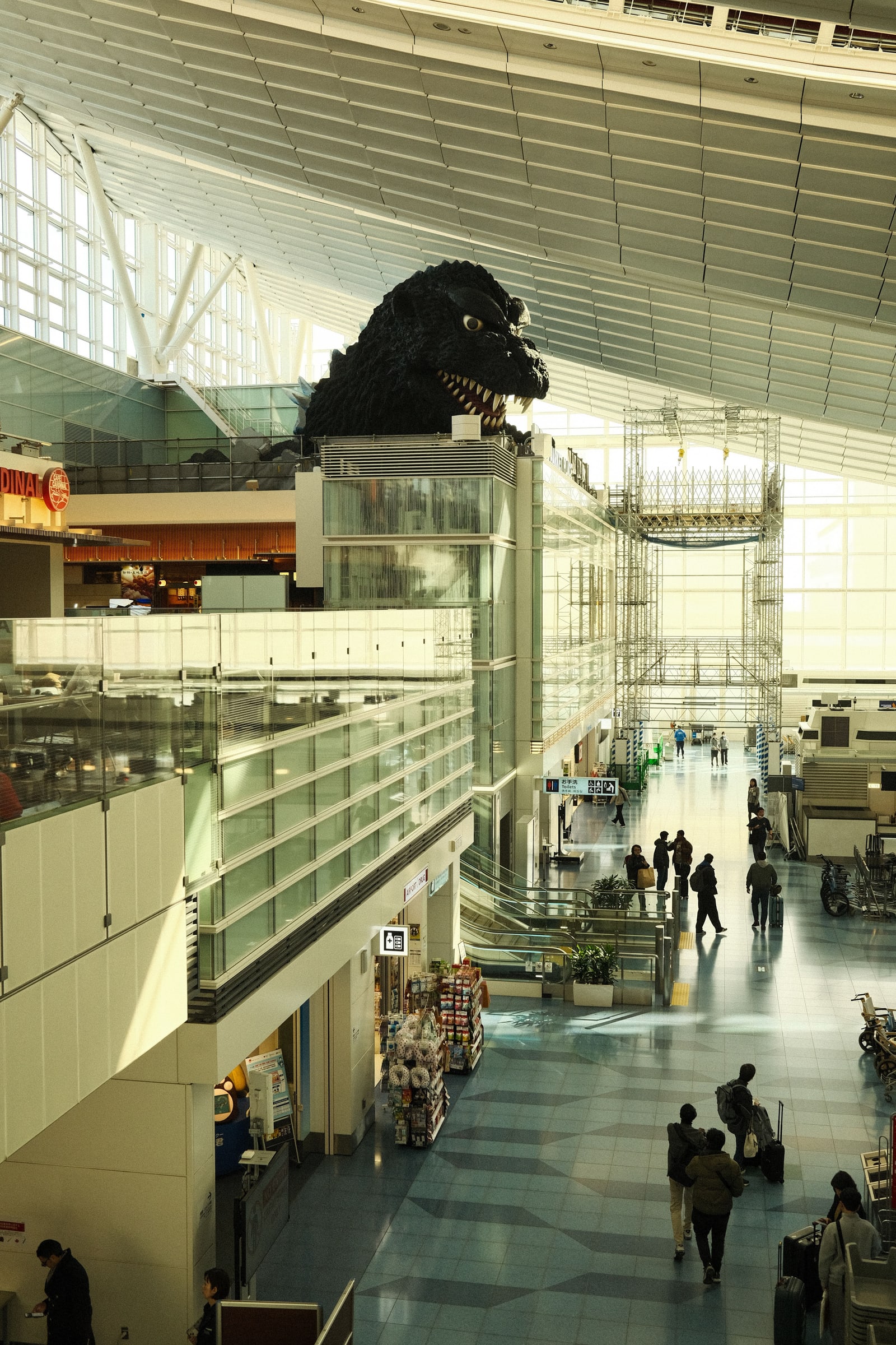 The large Godzilla head installation above the concourse of Haneda Airport Terminal 3, with travelers walking below.