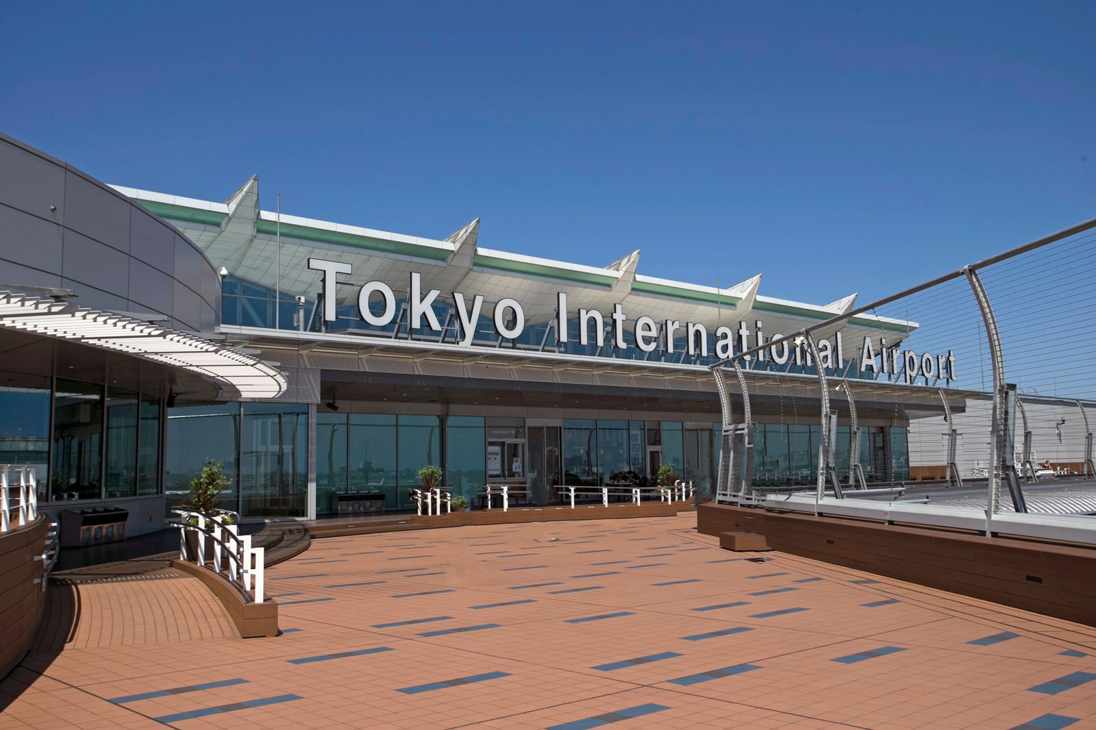The terminal entrance facade of Tokyo International Airport (Haneda), reading Tokyo International Airport above a covered forecourt, empty of people, under clear sky.