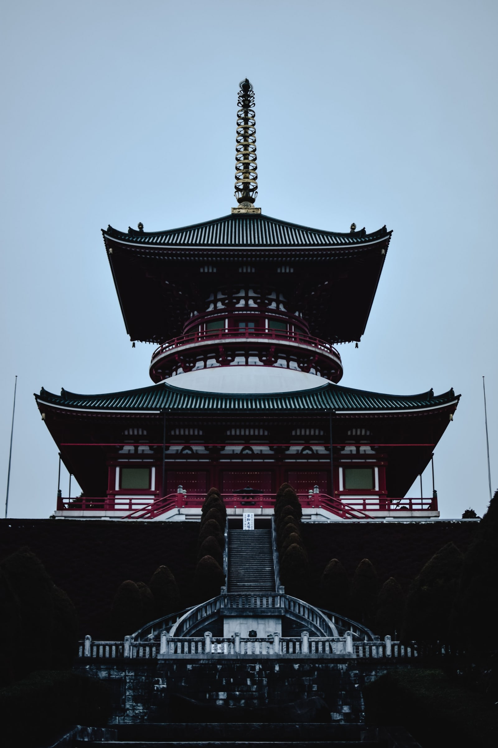 The Great Pagoda of Peace at Naritasan Shinshoji seen head-on above a flight of stone steps, red balconies and dark green roofs under a pale grey sky