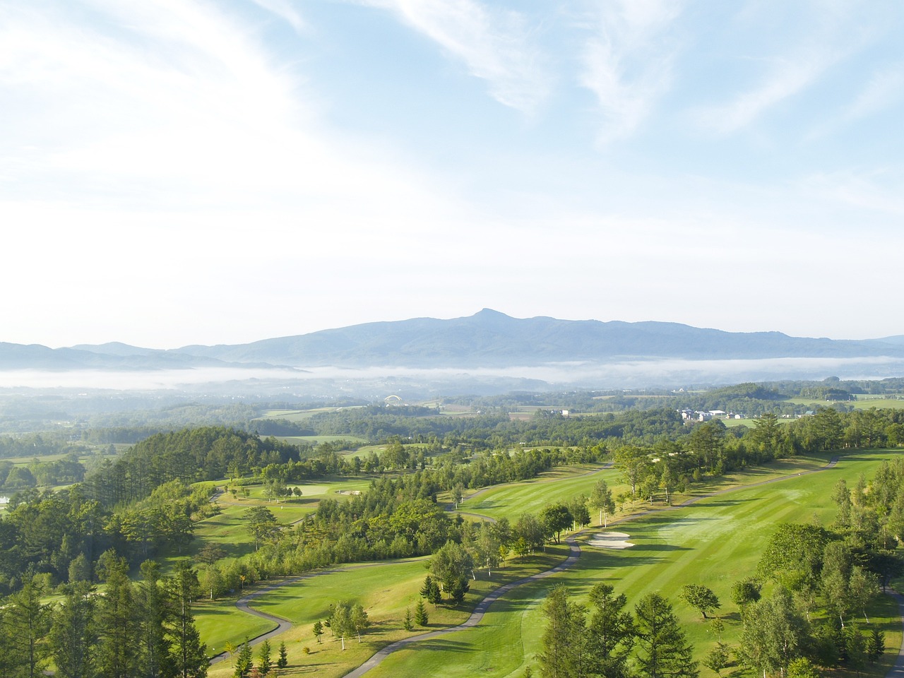 A green golf course with morning mist in the valley and a long ridge beyond, Niseko, Hokkaido