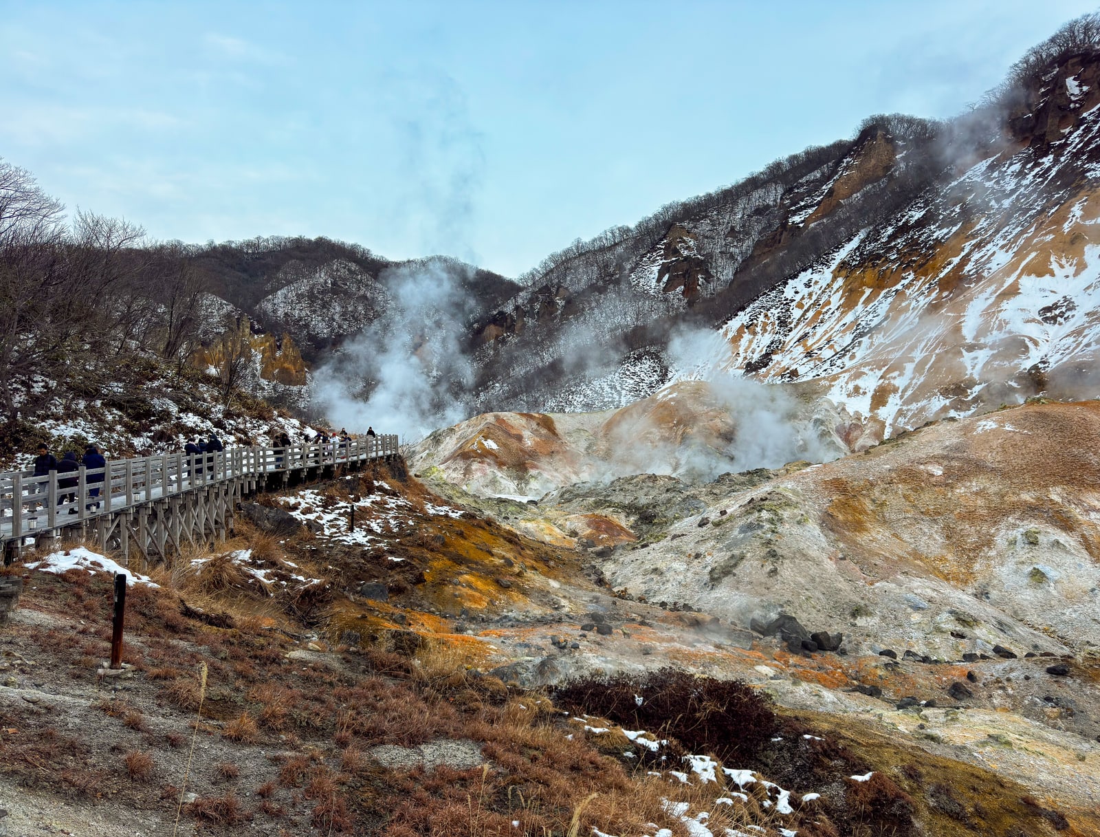 Visitors on a wooden boardwalk beside steaming vents in a snow-dusted volcanic valley, Noboribetsu