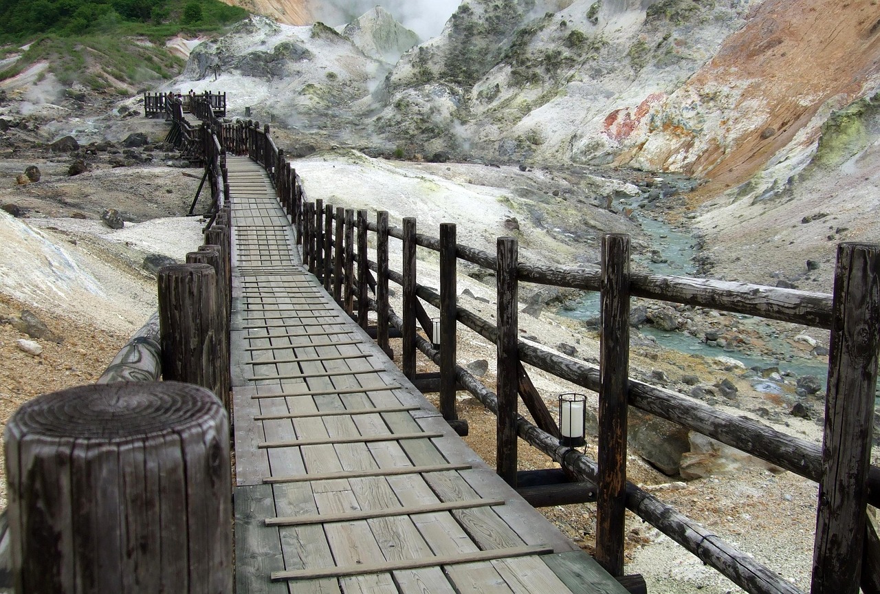 A wooden boardwalk through a sulphur valley beside a pale blue-green stream, Noboribetsu