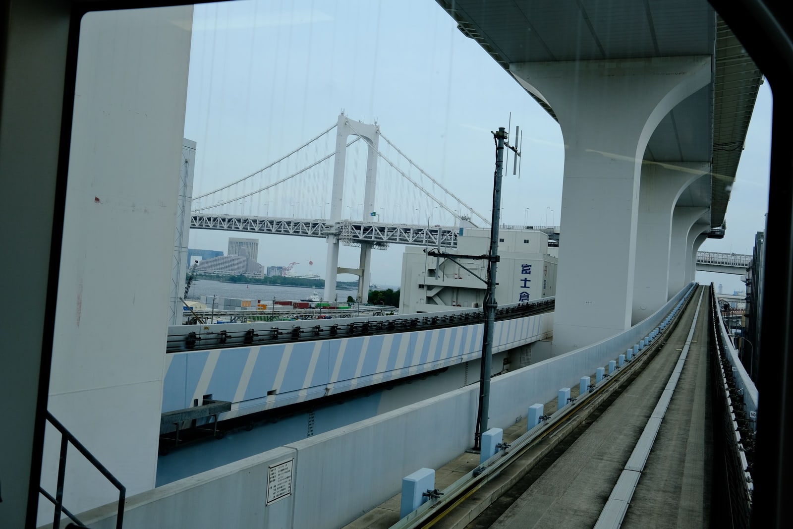 The Rainbow Bridge seen through the front window of a train on an elevated guideway, warehouses below