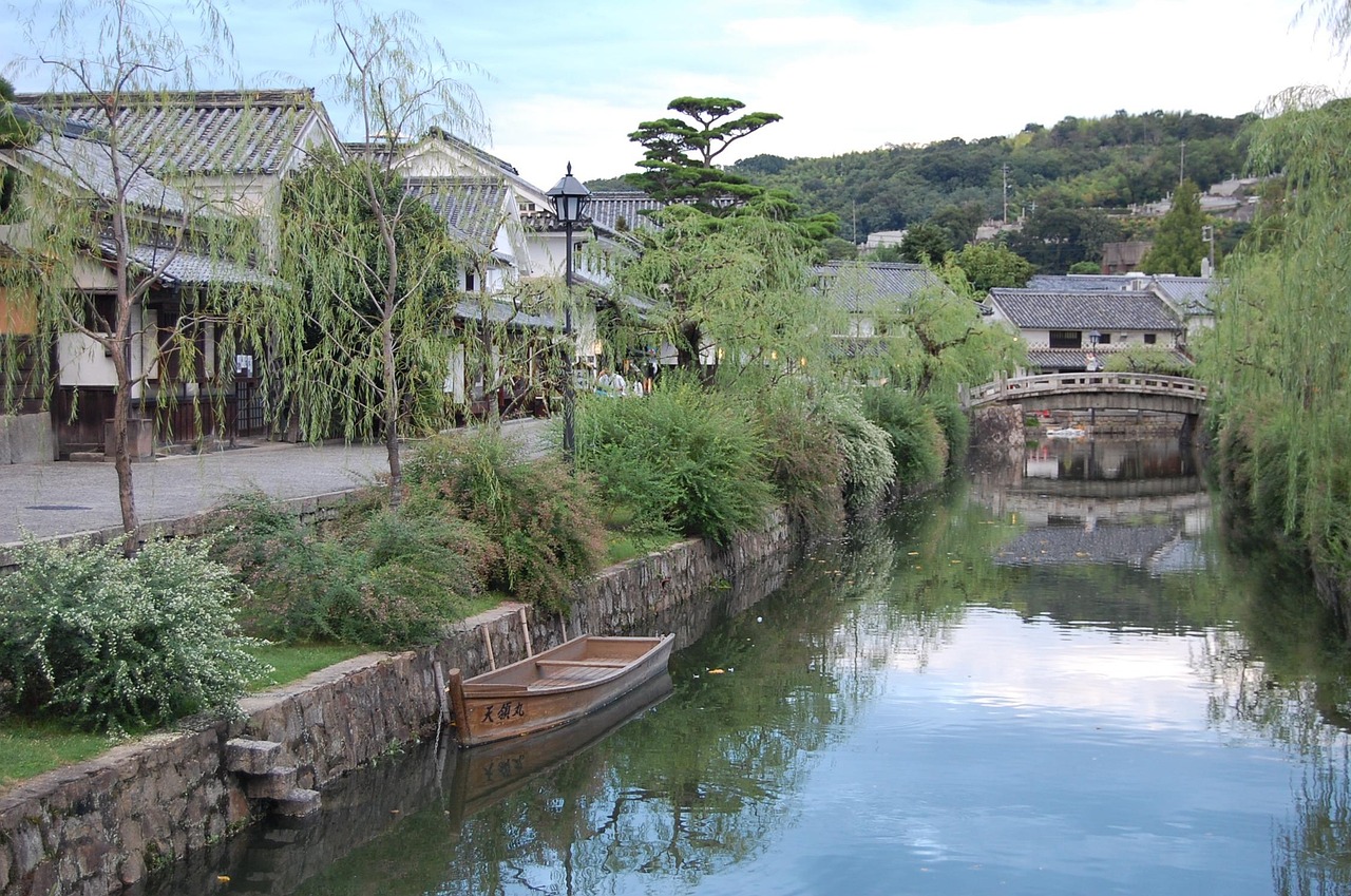 The canal in the Kurashiki Bikan Historical Quarter, weeping willows along the bank and a wooden boat moored by the stone wall