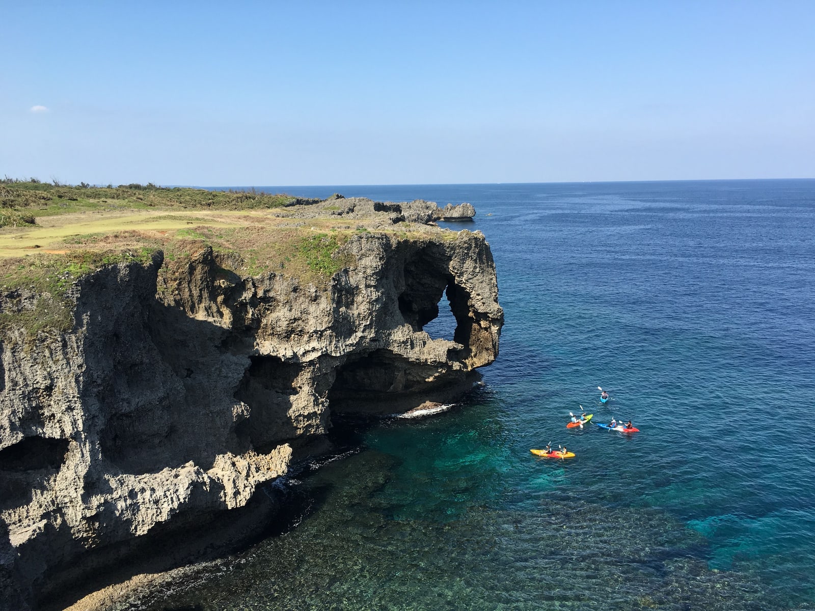 The cliff at Cape Manzamo above turquoise water, with kayaks below it.