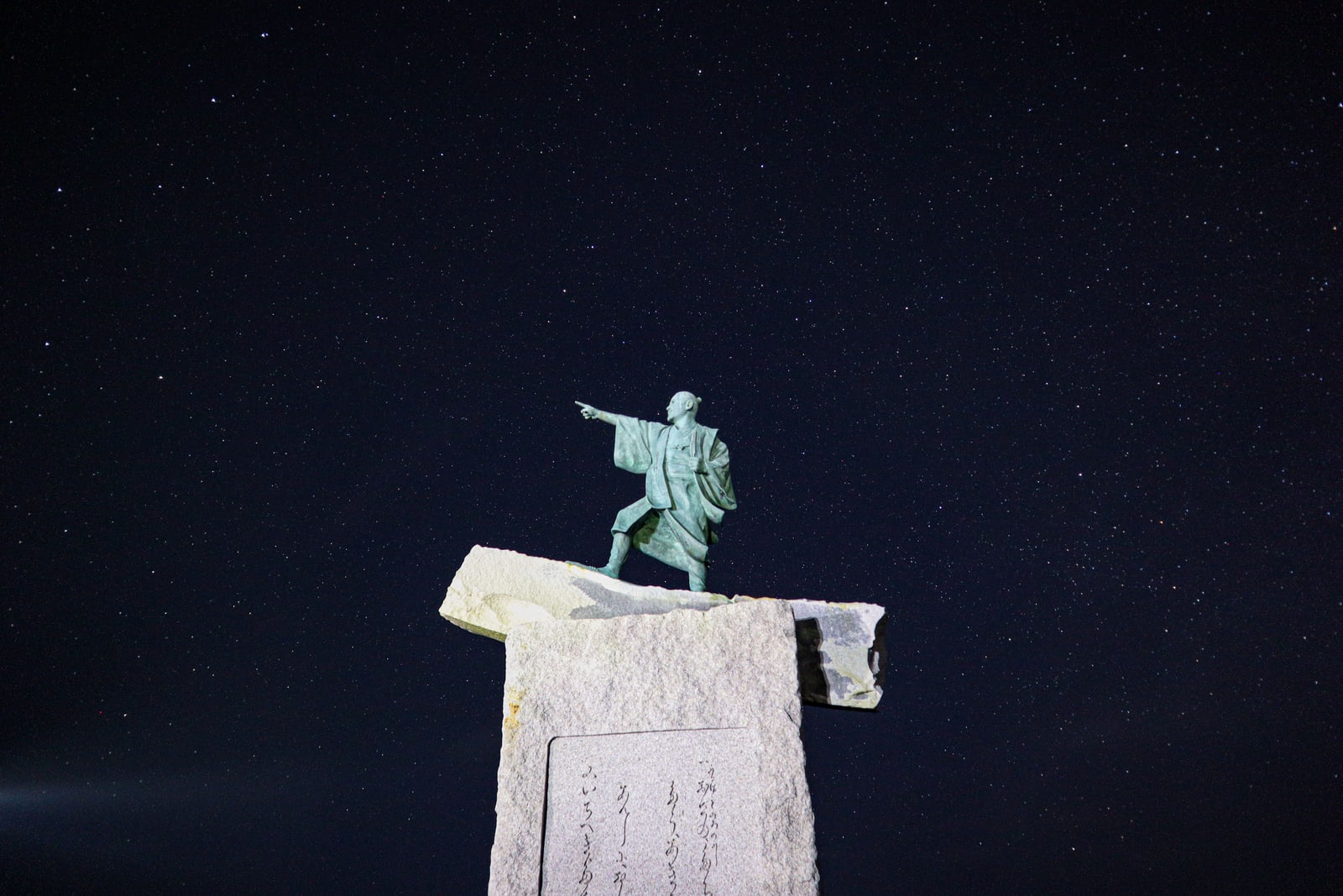 The bronze statue of Taiki pointing out to sea, on a granite monument at Cape Zanpa under a night sky full of stars