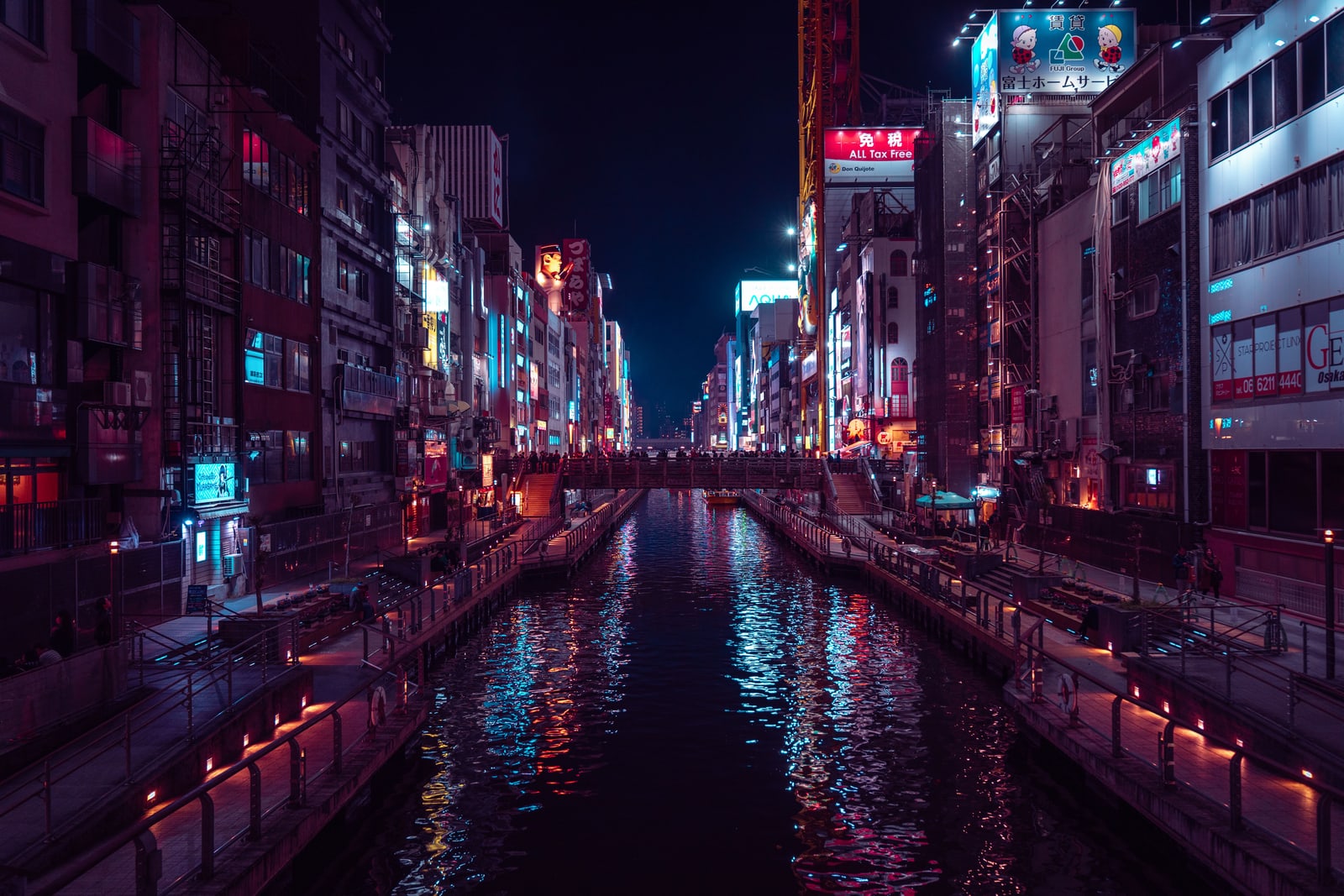 The Dotonbori canal in Osaka at night, lit buildings on both banks reflected in the water and a bridge in the distance.