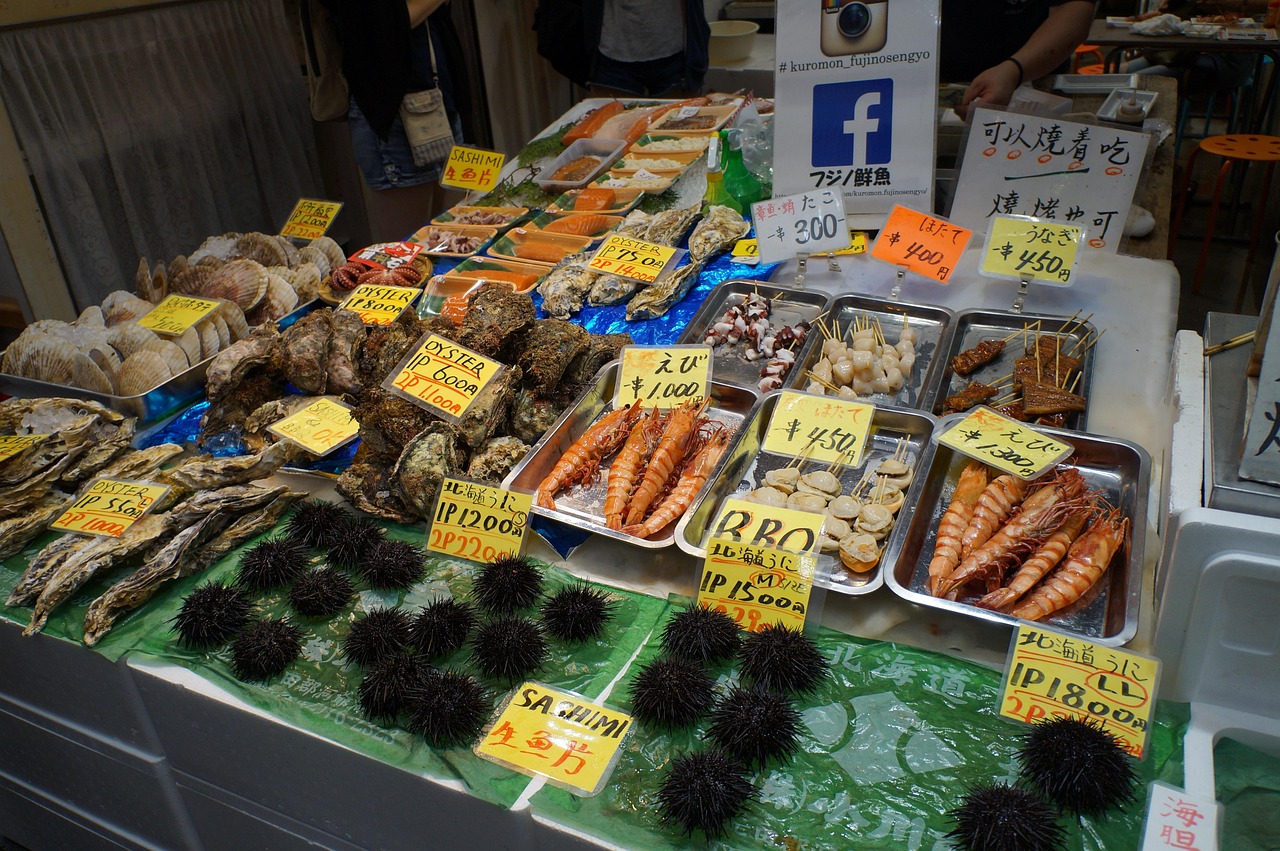 A Kuromon Market stall counter with sea urchins, grilled shellfish and prawns on ice, with handwritten yen price tags.