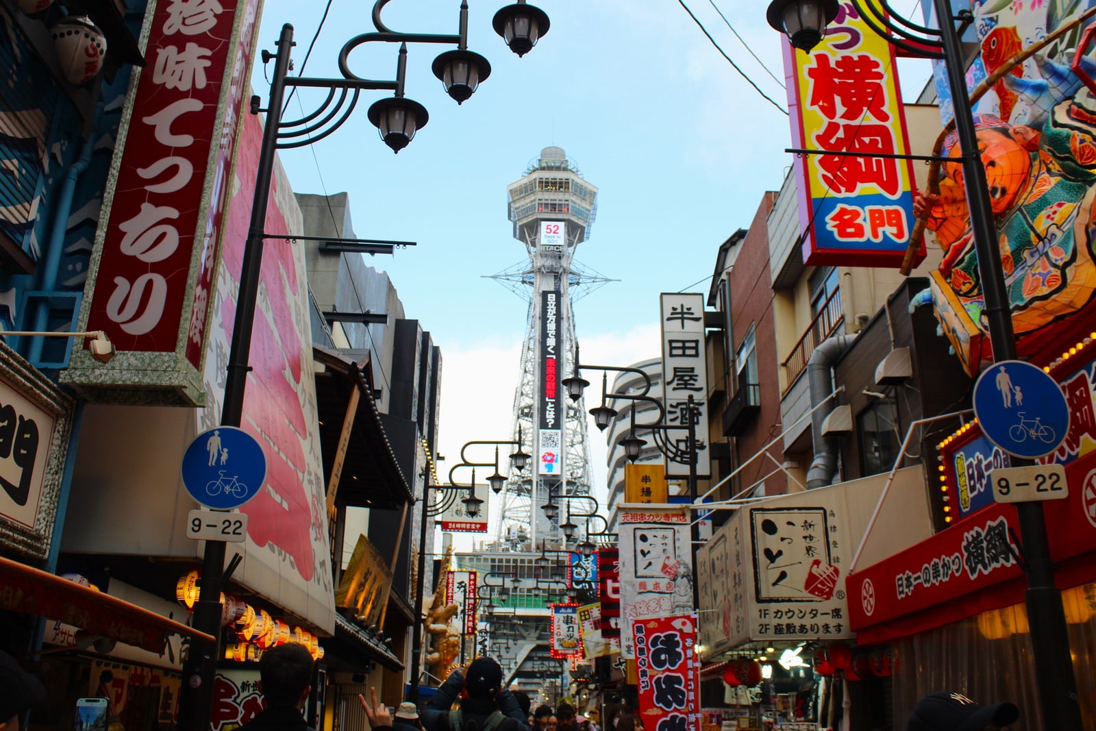 Tsutenkaku tower at the end of a Shinsekai shopping street lined with shop signs and street lamps.