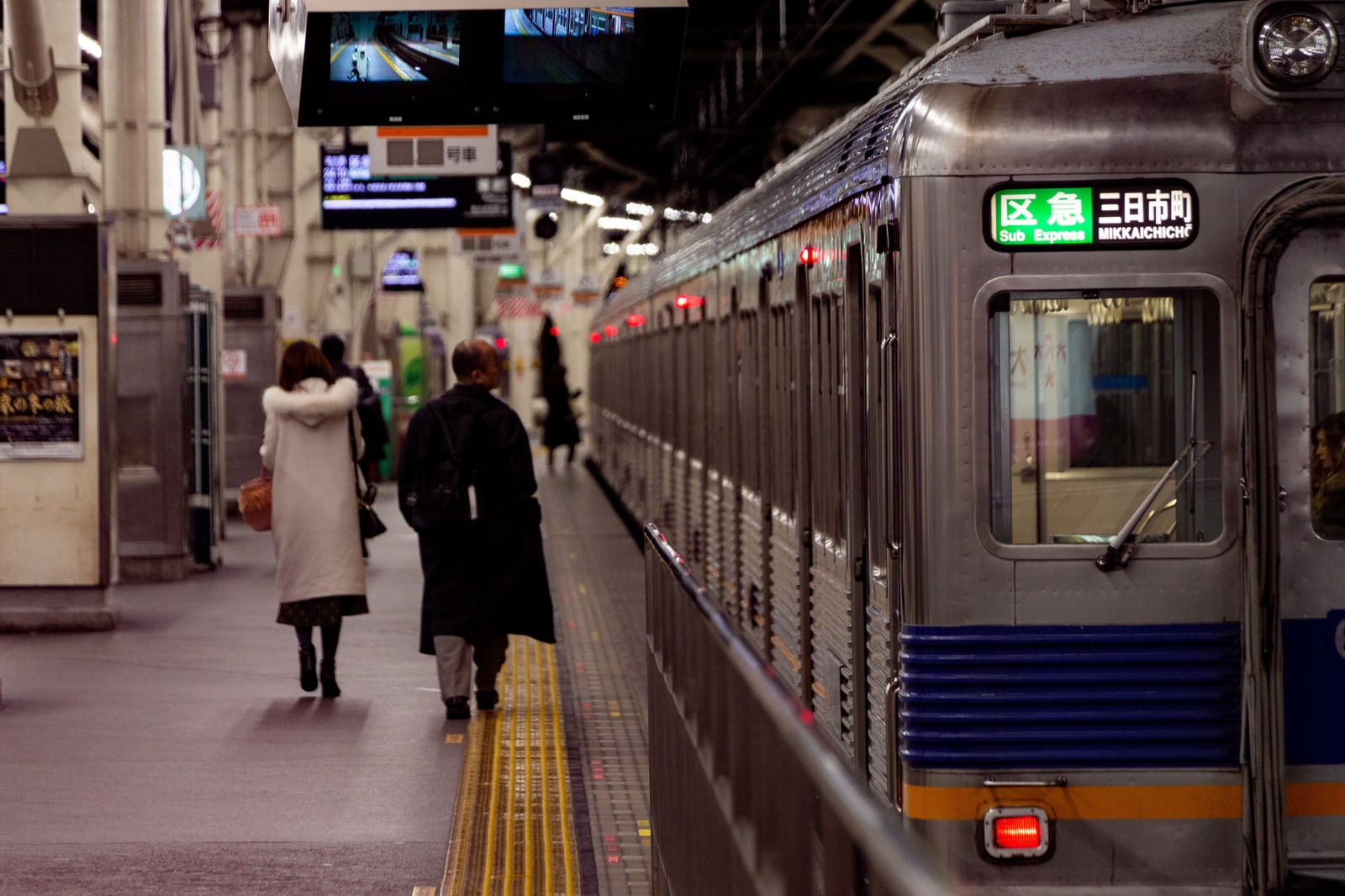 A silver Nankai train at a platform in Osaka with two commuters walking alongside it.