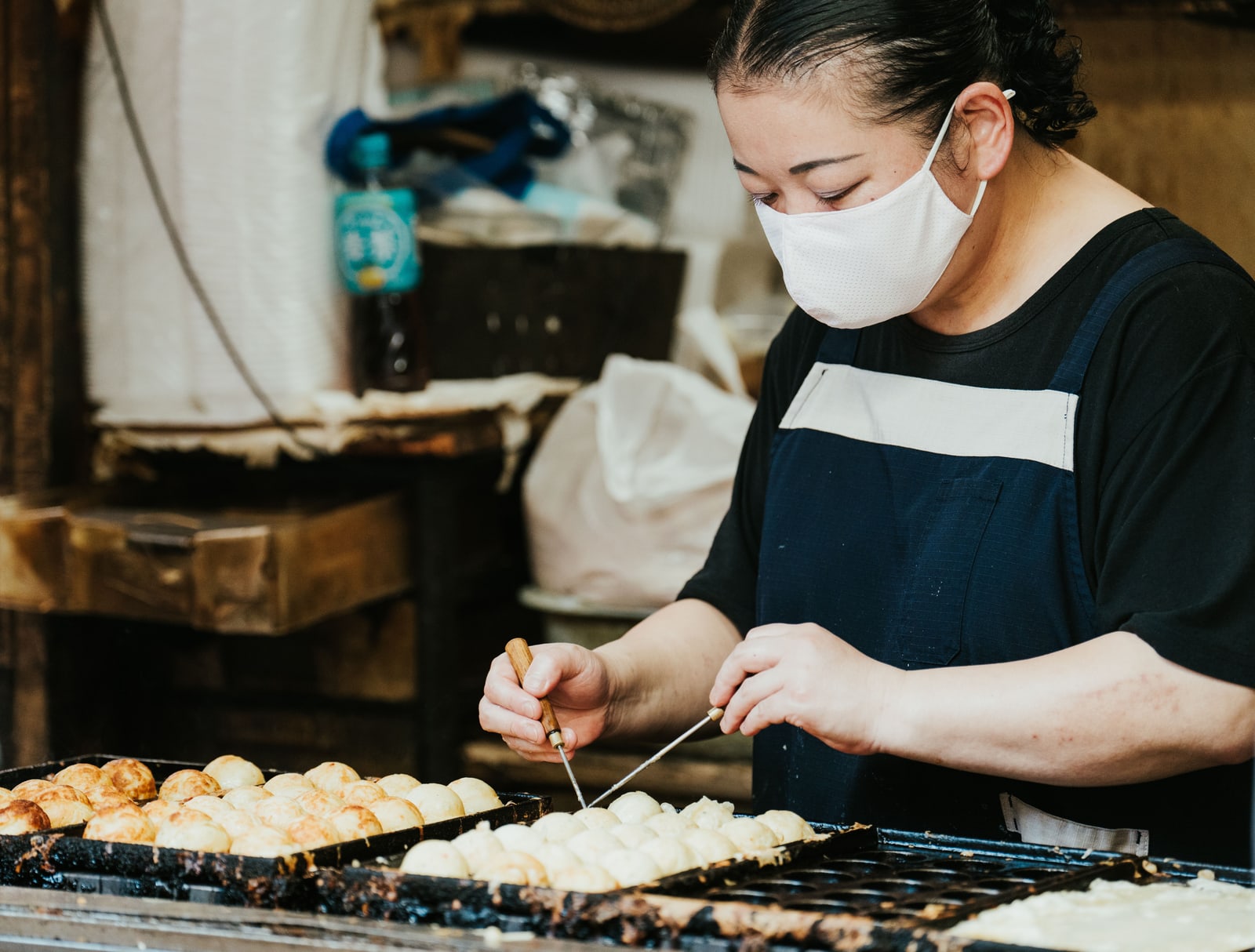 A vendor turning takoyaki on an iron griddle with two picks.