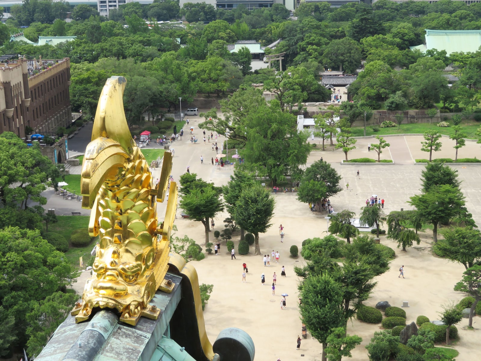 Looking straight down from the top of the tower past a gold roof fish onto the square and paths, with small figures of visitors.
