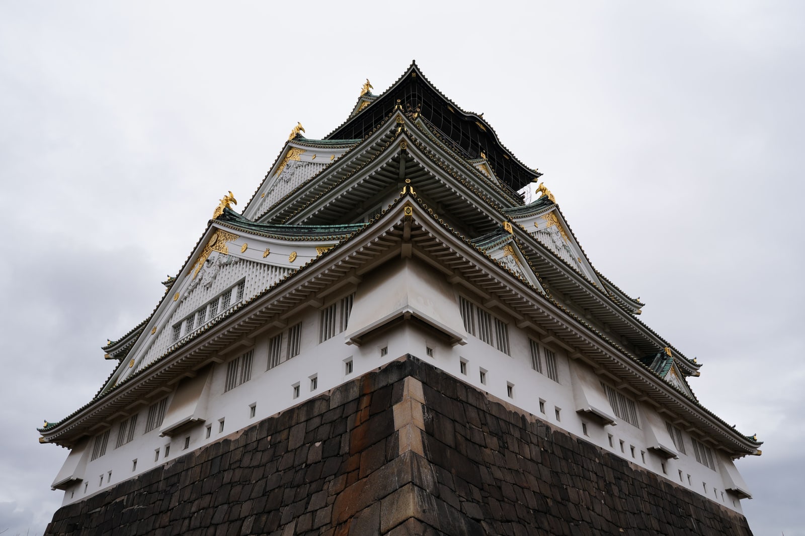 The main tower seen from directly below its stone base, white walls, green roofs and gold trim against a gray sky.