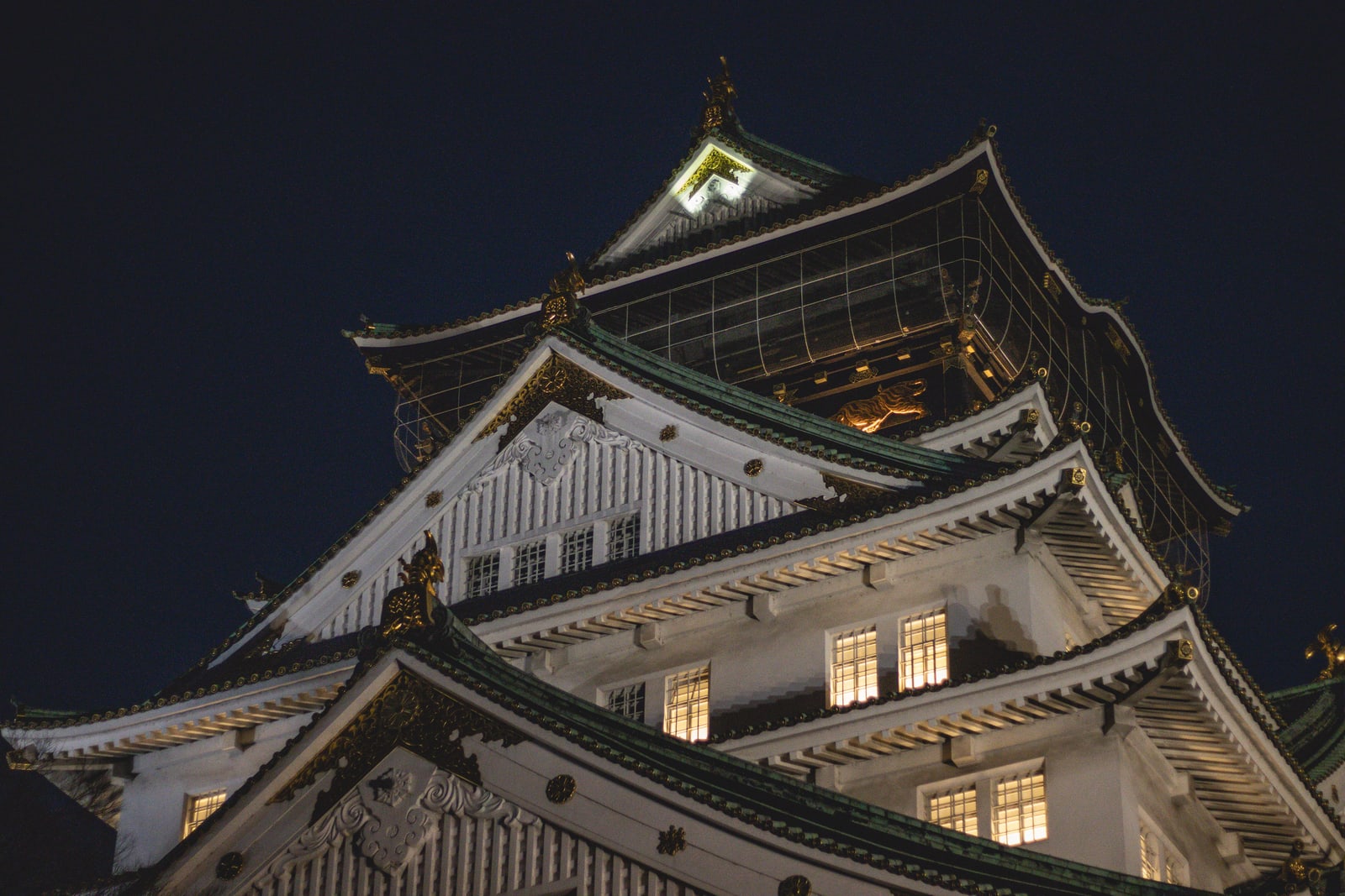 The upper roofs of Osaka Castle's main tower lit up against a black night sky.
