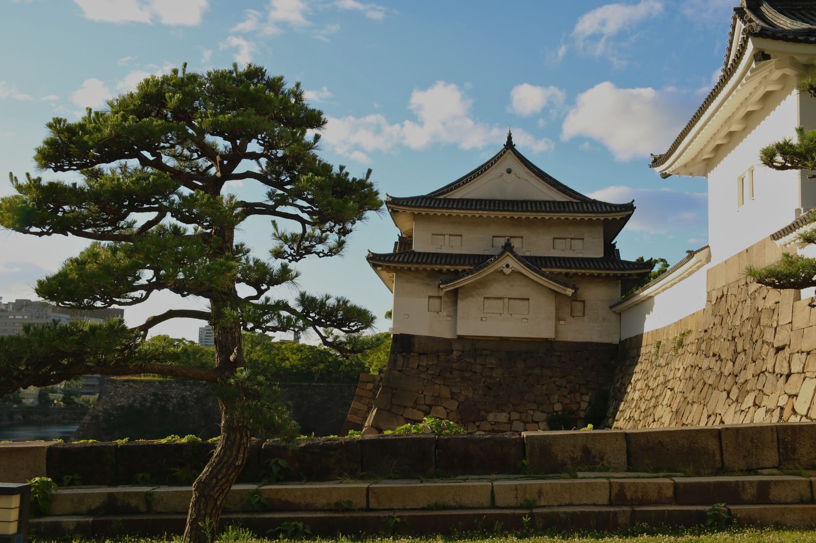 A two-story white corner turret on a stone base with a shaped pine tree in front of it.