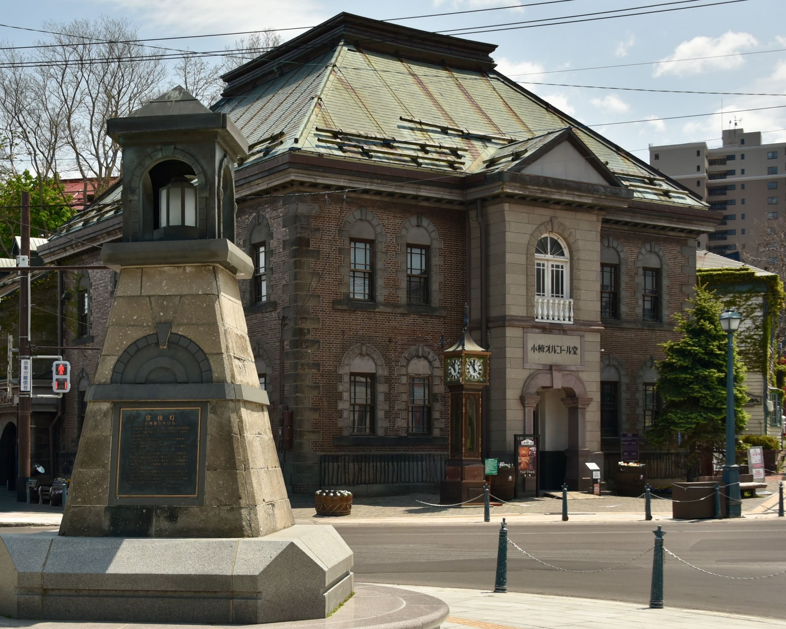 The brick building with the 小樽オルゴール堂 sign and the clock beside its entrance, on a clear day