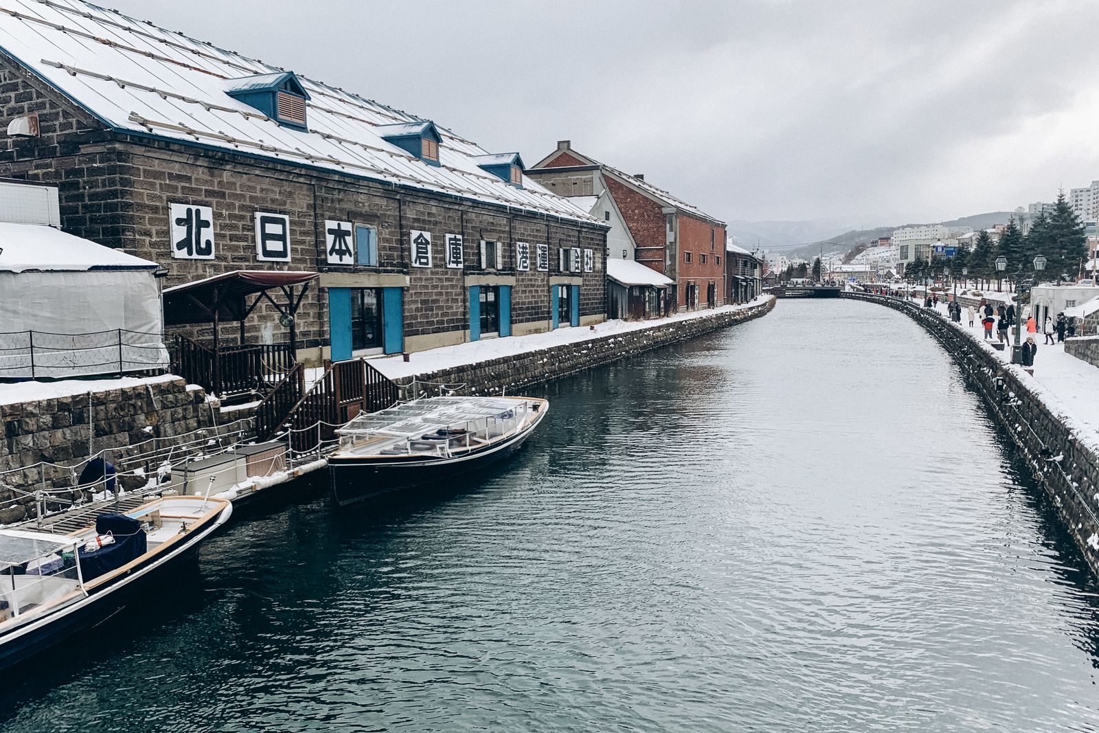 Otaru Canal on an overcast winter day, boats moored beside snow-dusted stone warehouses