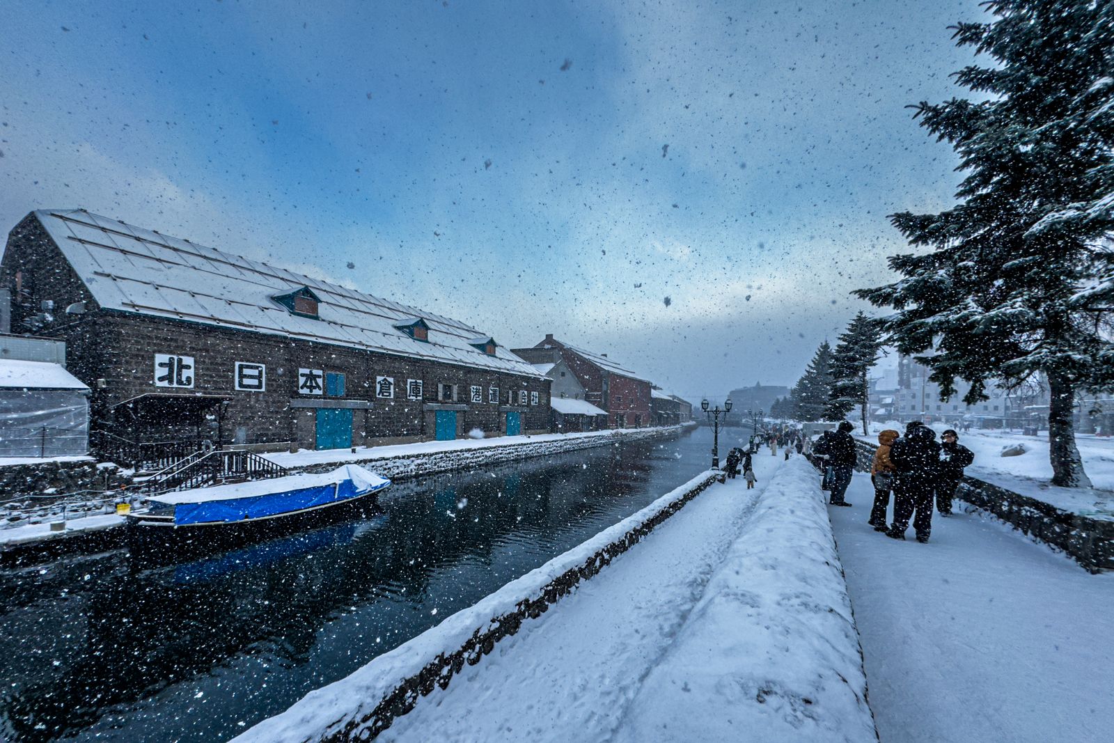 Otaru Canal in heavy snowfall, a stone warehouse and street lamps along the snowy towpath