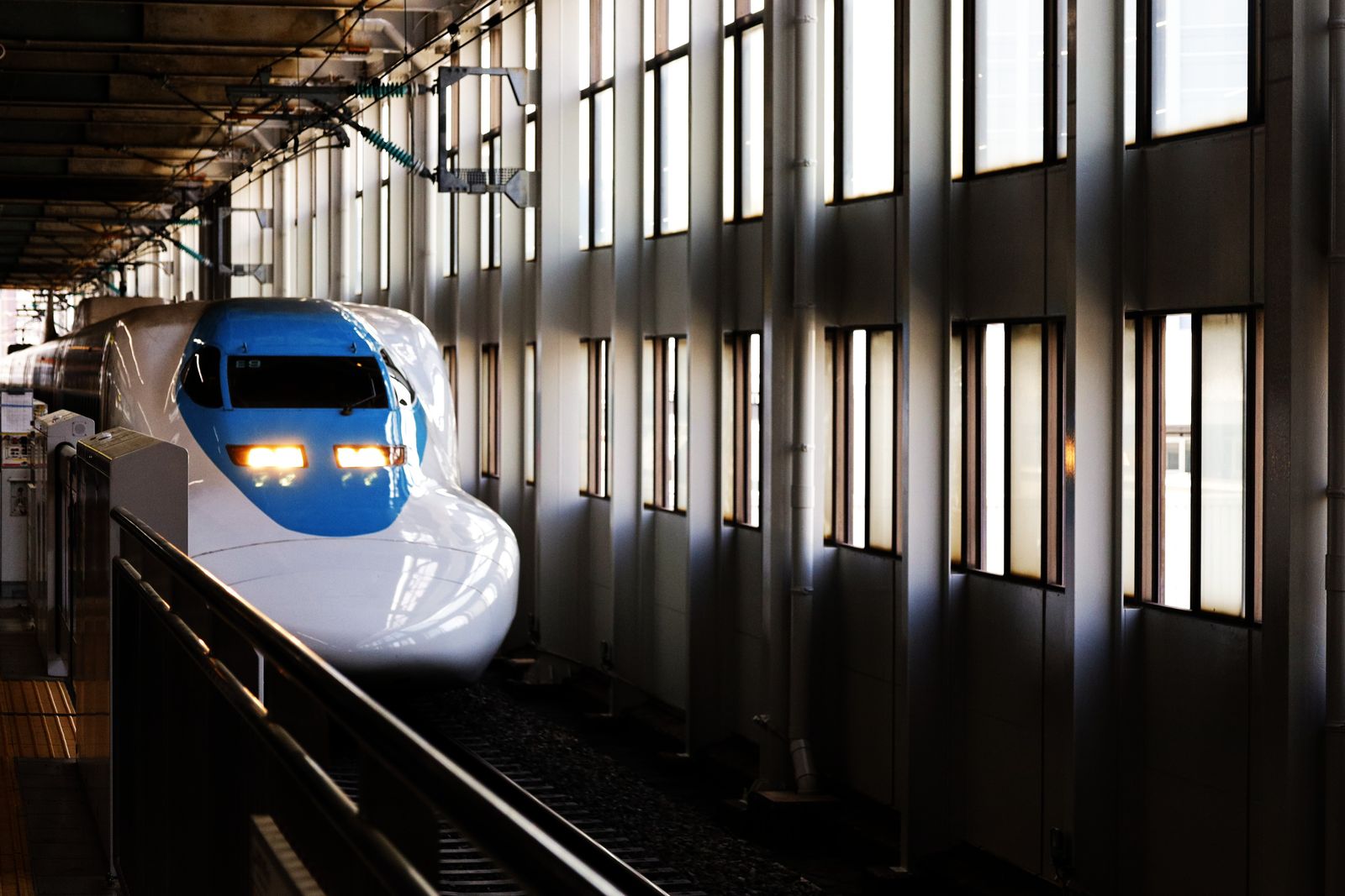 A blue-nosed shinkansen arriving at Hiroshima Station under the platform canopy.