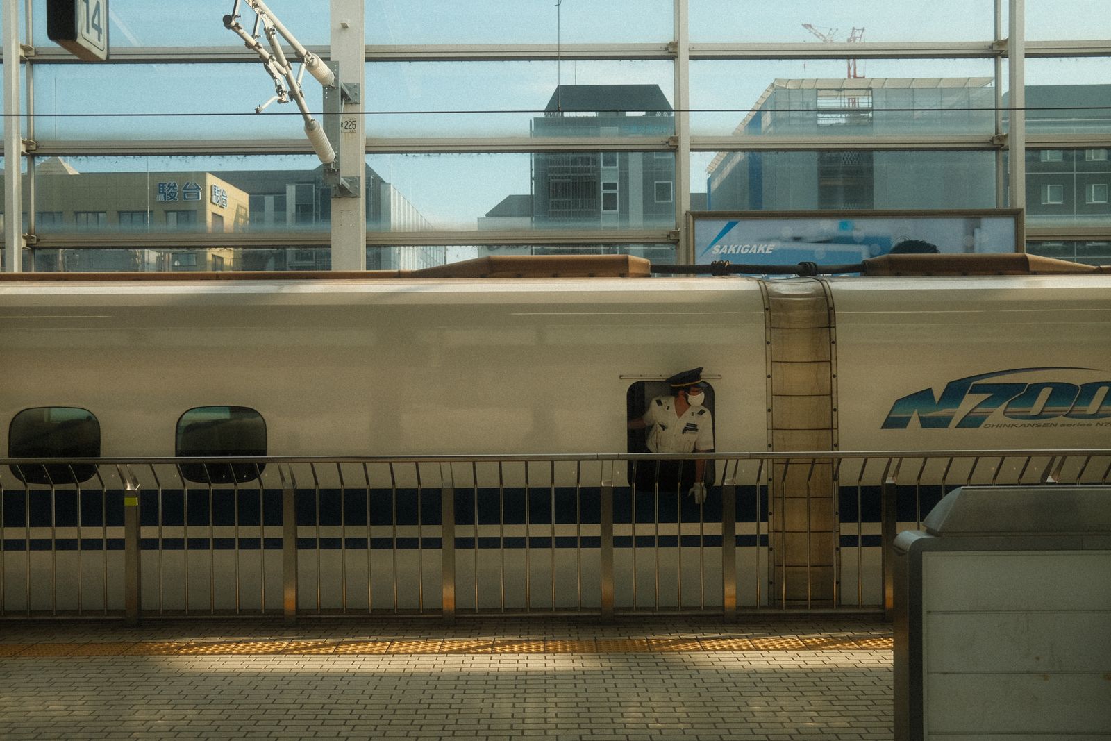 An N700-series shinkansen at a Tokyo platform, a conductor leaning from the crew door.