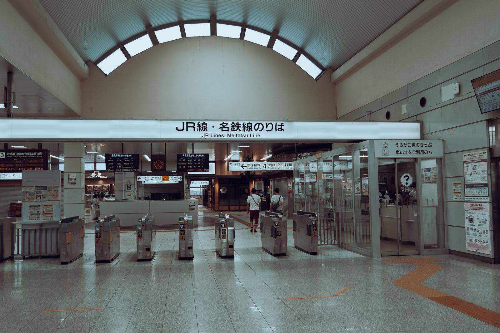 A line of JR ticket gates under a sign reading JR Lines and Meitetsu Line, sharing one station concourse.