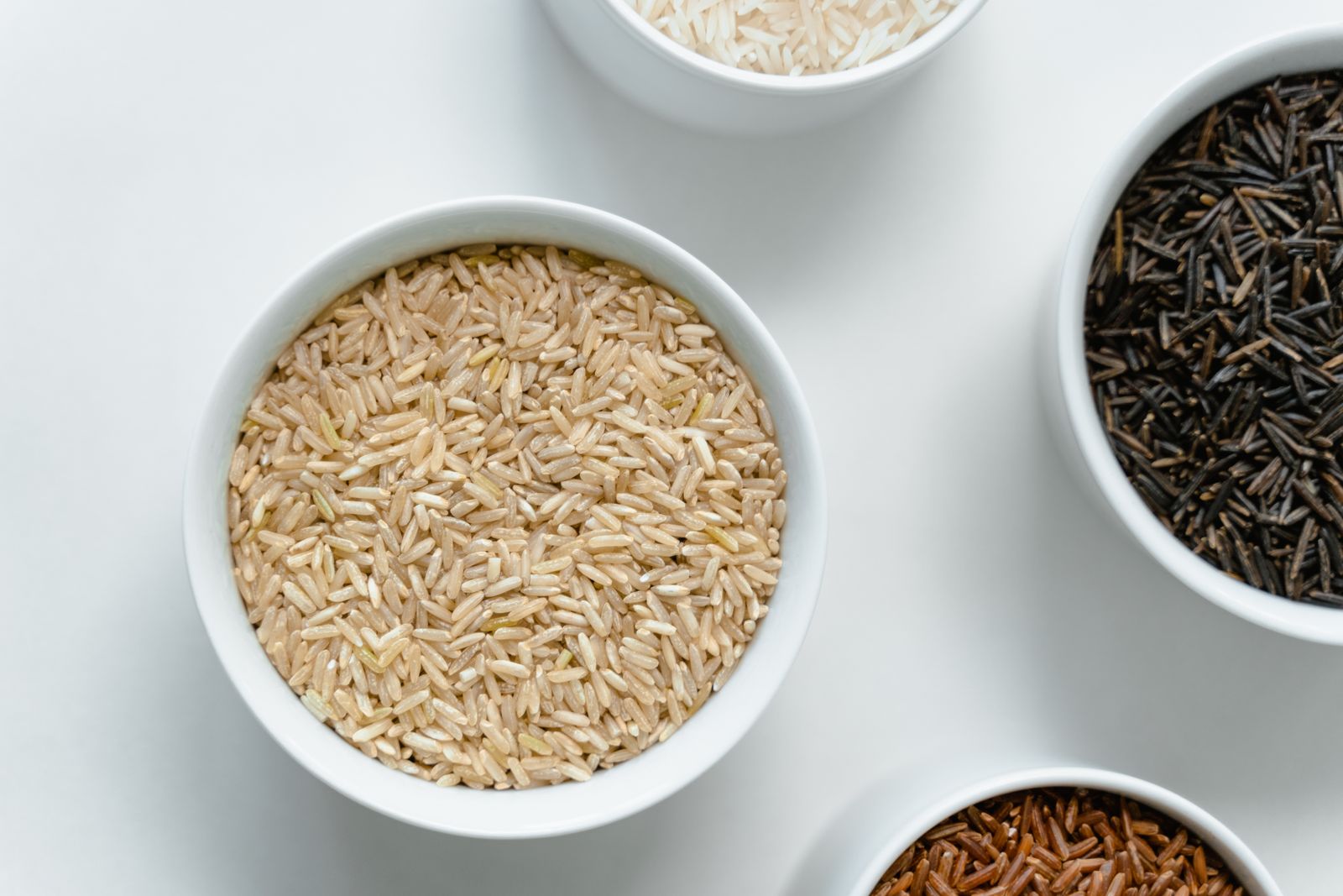 Several kinds of rice and grain in white ceramic bowls.