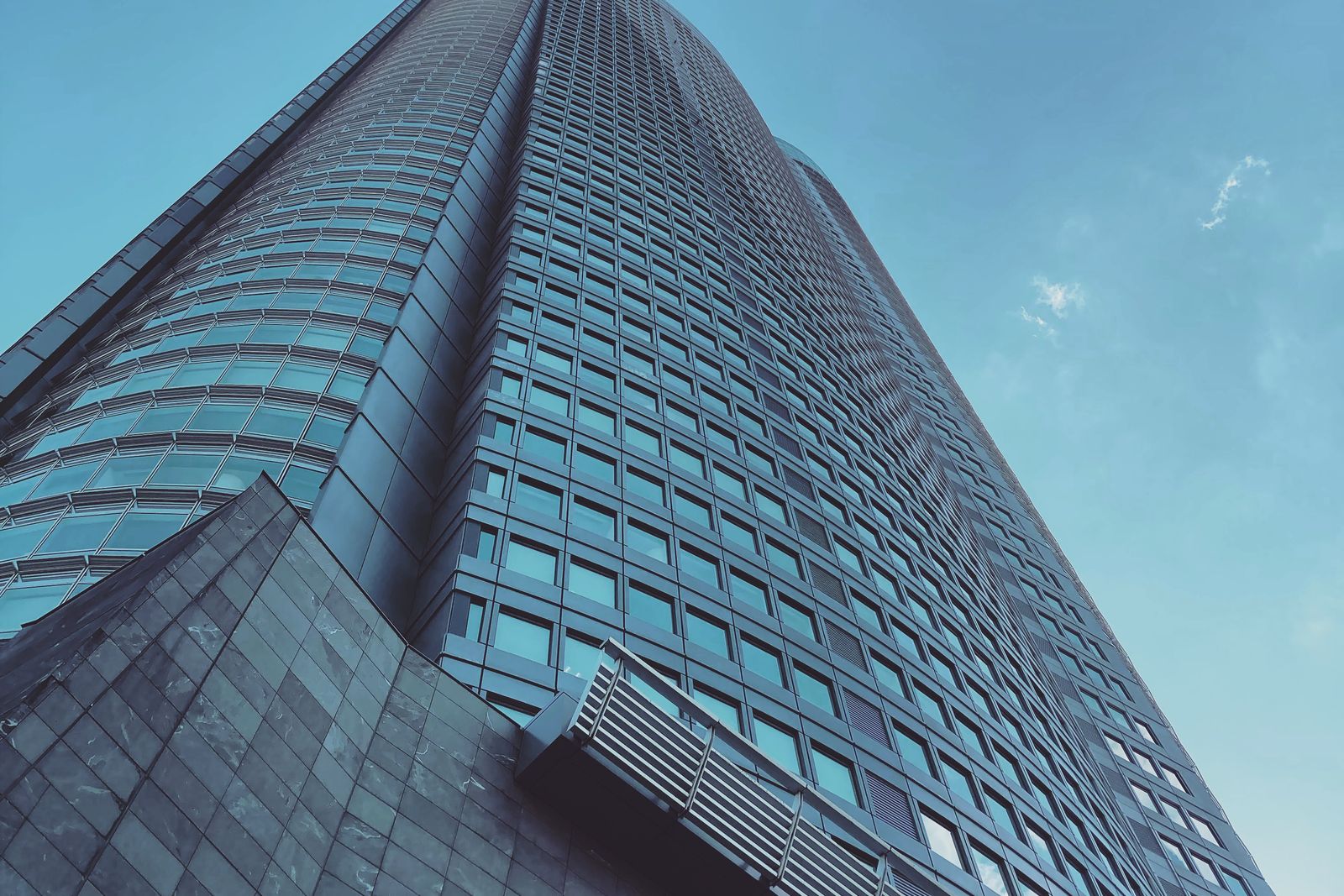 The Roppongi Hills Mori Tower seen from below, glass and steel against a clear blue sky