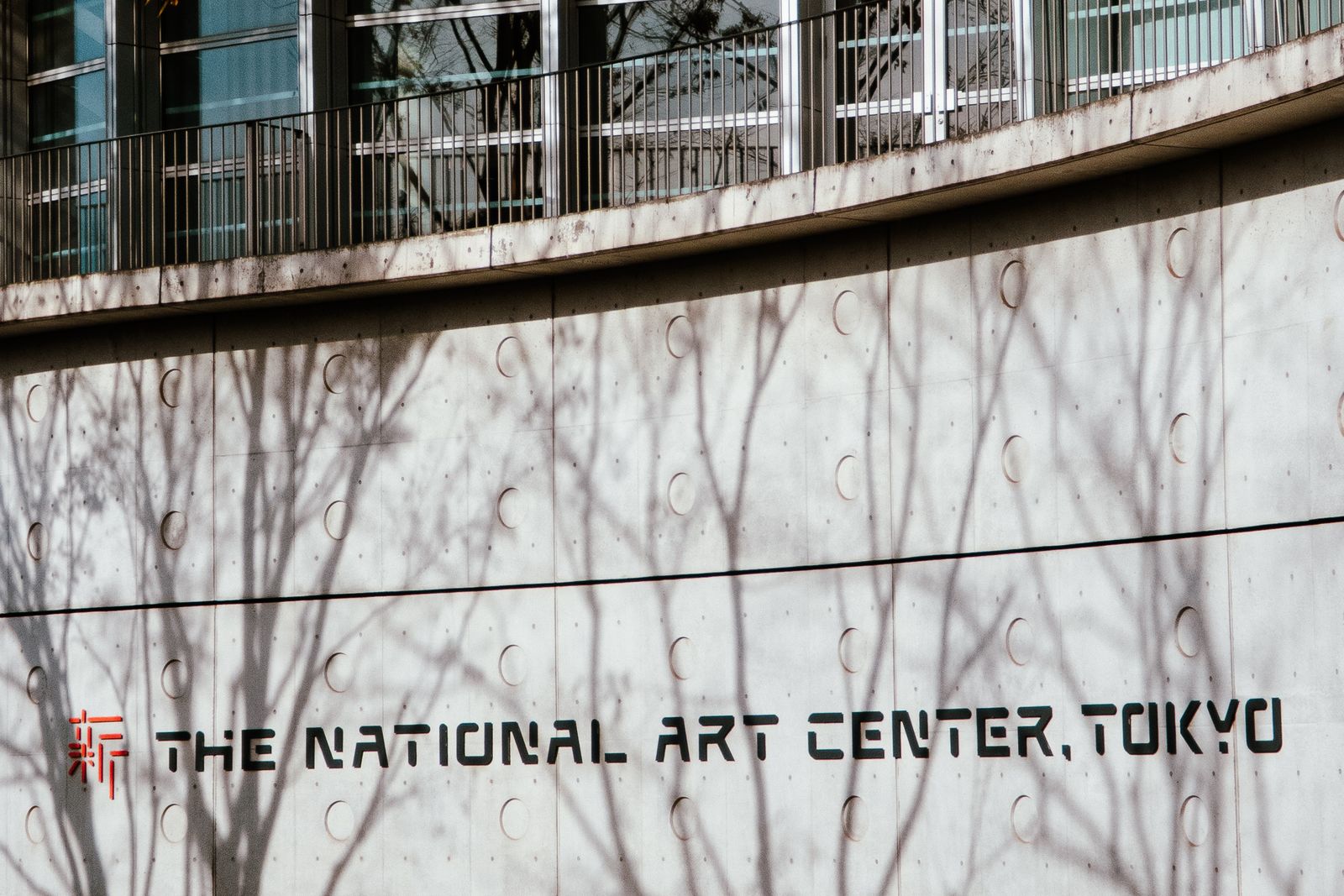 The lettering THE NATIONAL ART CENTER, TOKYO on a curved concrete wall, with shadows of bare branches