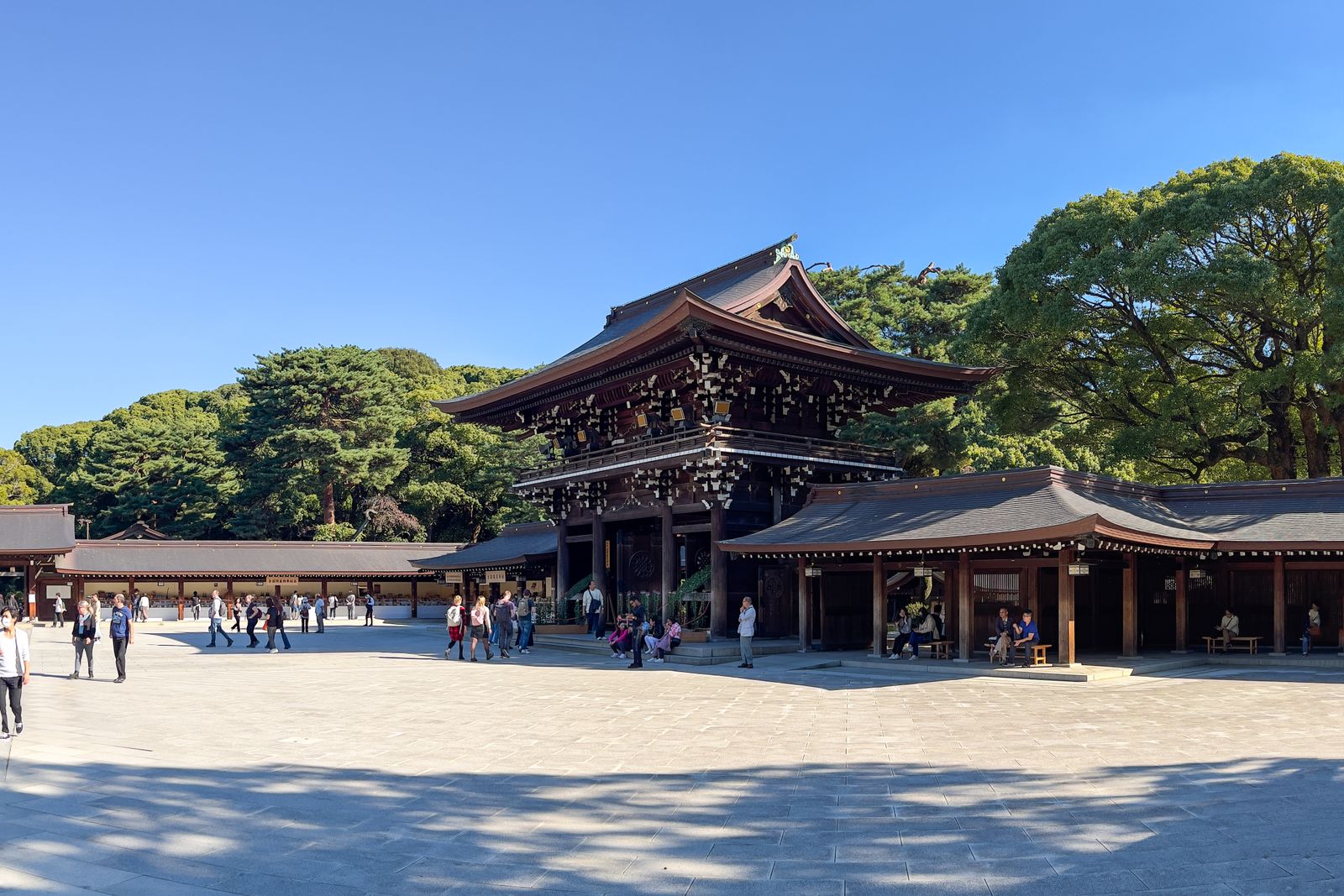 A shrine courtyard in Tokyo with visitors crossing it on a clear day.