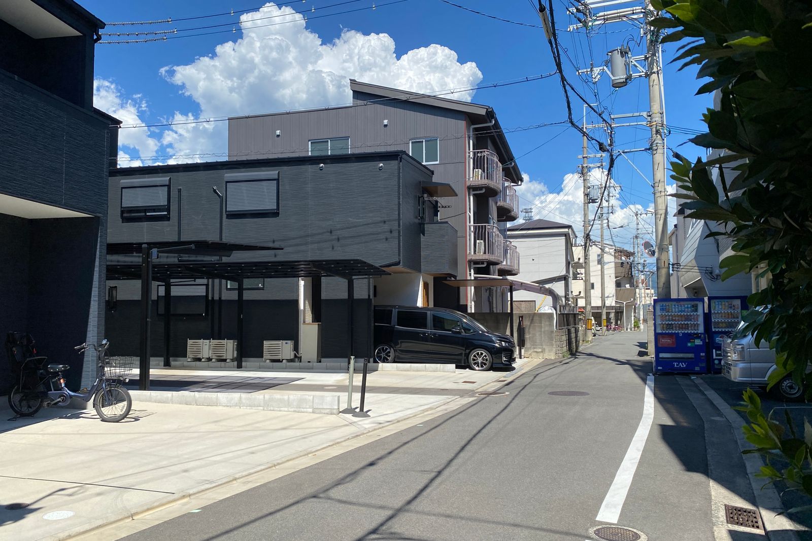 A Japanese residential street on a clear day, power lines overhead and vending machines down the block.