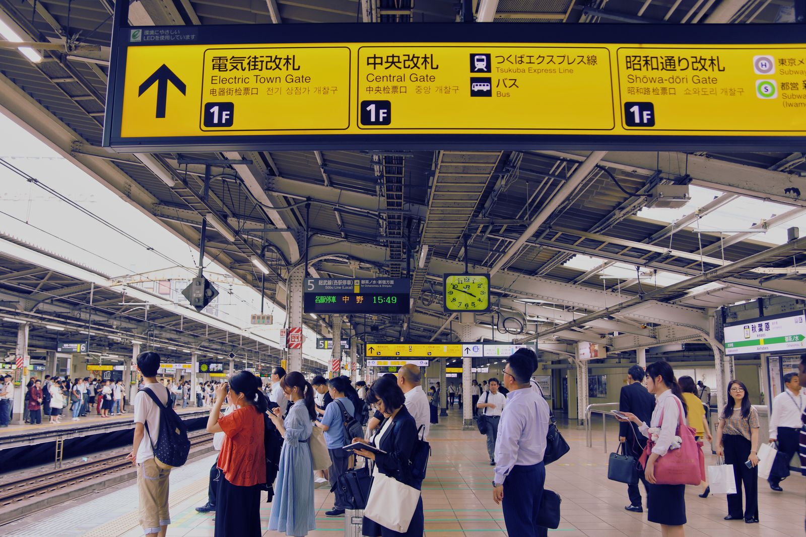A crowded Akihabara platform under four-language gate signage, commuters spread along the platform edge.