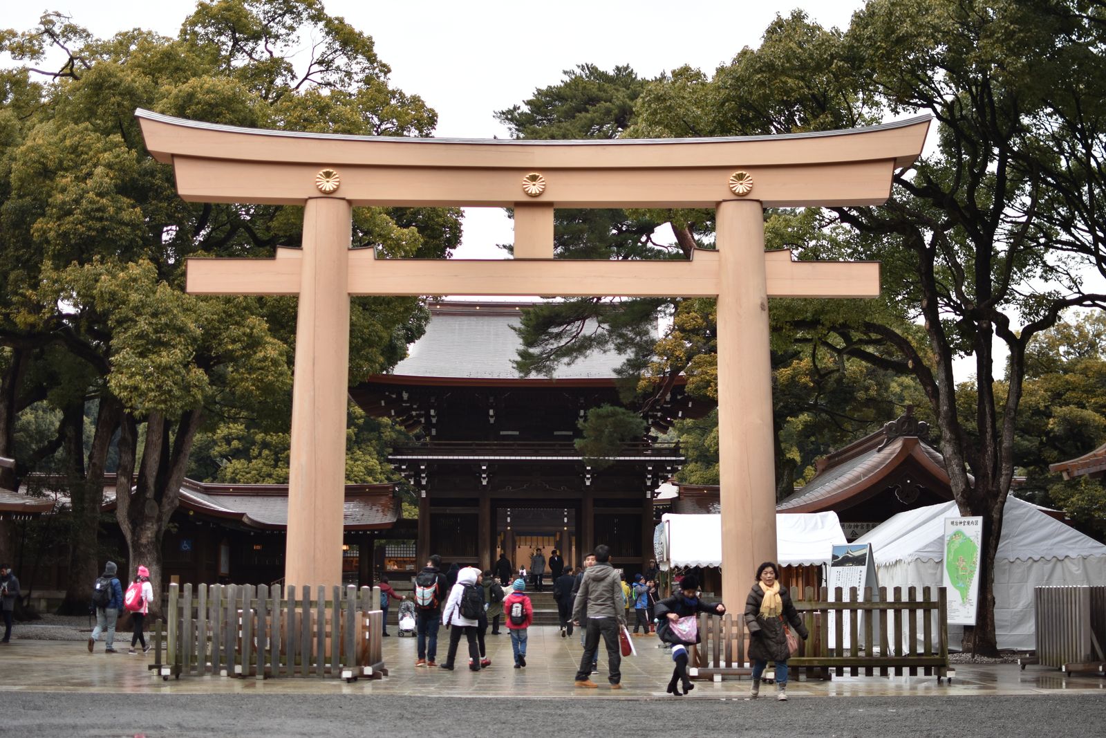 A wooden torii gate with chrysanthemum crests, people walking through in ordinary clothes.