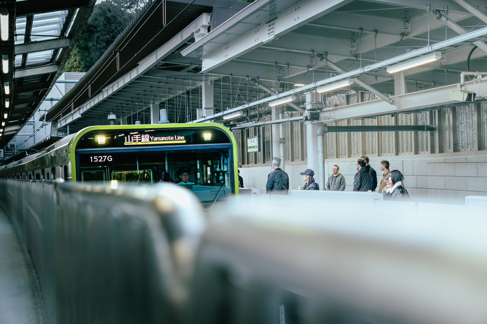 A Yamanote Line train arriving at a Tokyo platform with passengers waiting back from the edge.