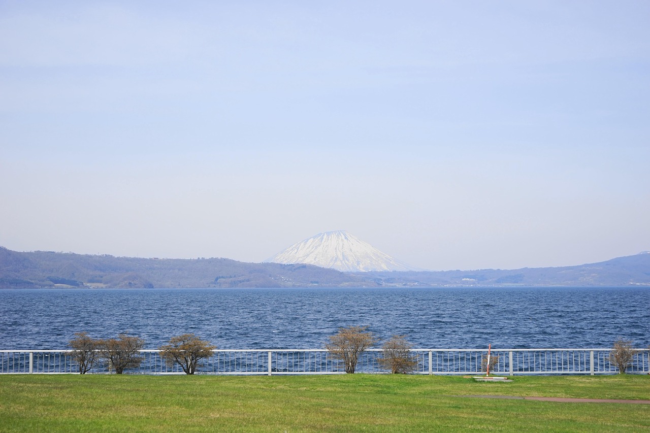 A snow-capped volcano behind Lake Toya, seen across a lawn and a white railing, Hokkaido