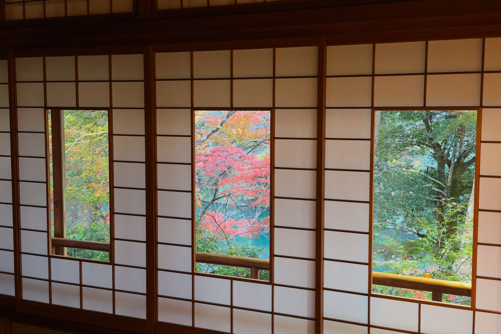 Three shoji screens with their lower panels slid open onto autumn maples and a river below.