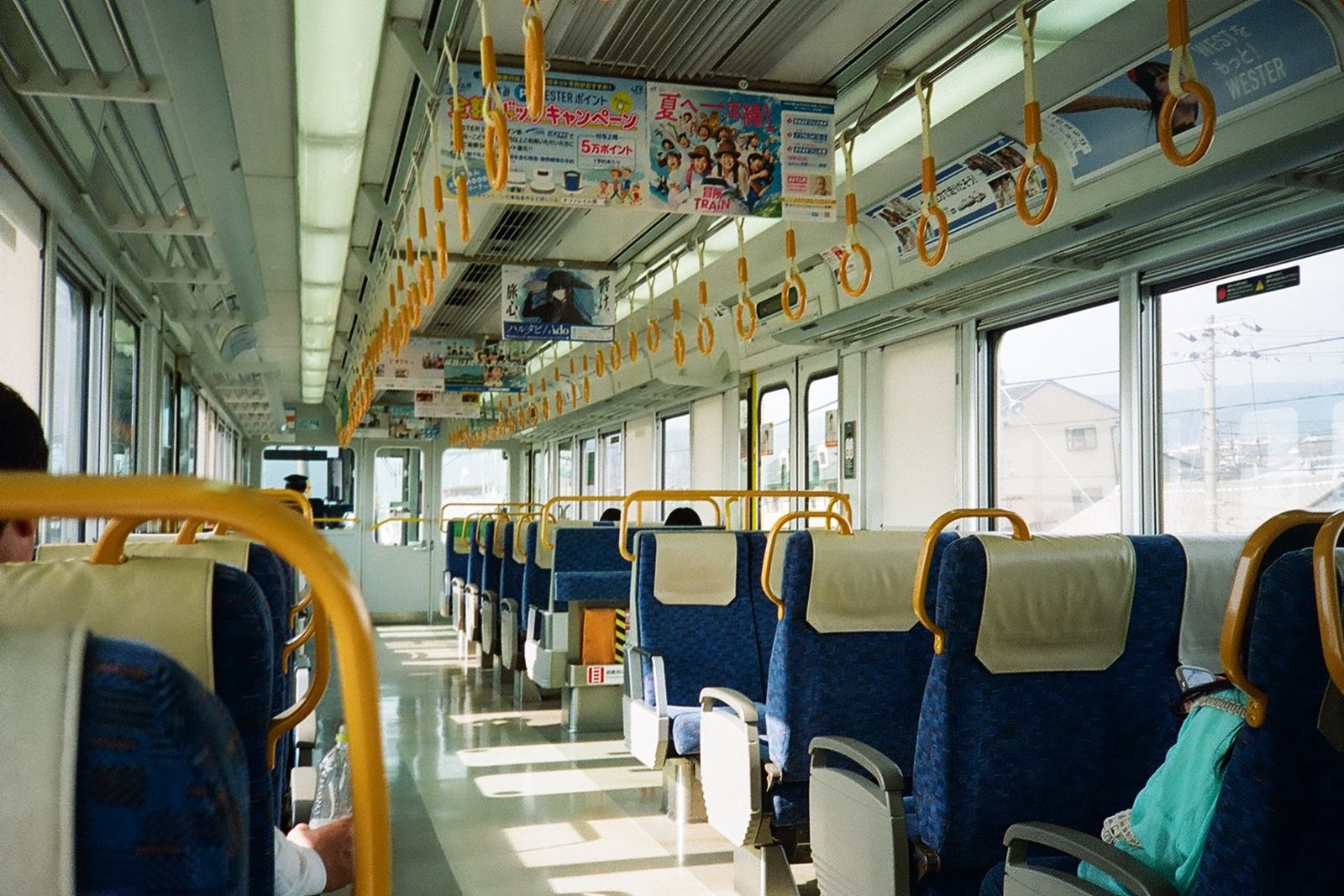 The interior of a near-empty Japanese local train in daylight, handrails and empty seats.