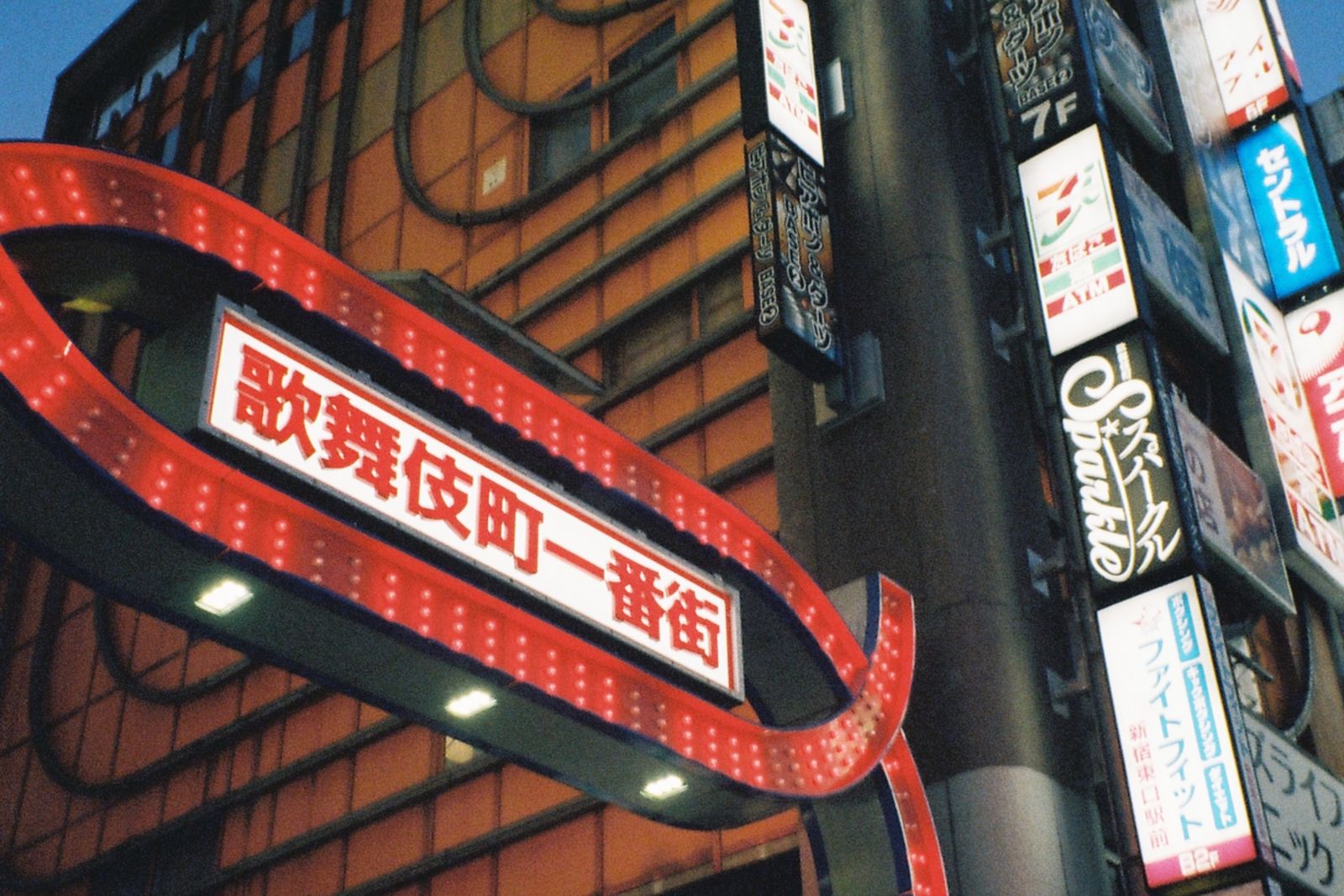 The red illuminated Kabukicho Ichibangai arch at dusk, with stacked shop signs beside it