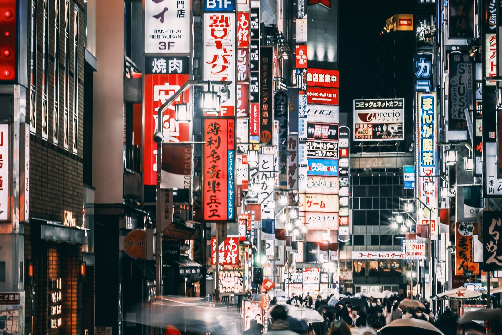 A Shinjuku street at night under illuminated signage, pedestrians blurred by motion and unidentifiable.